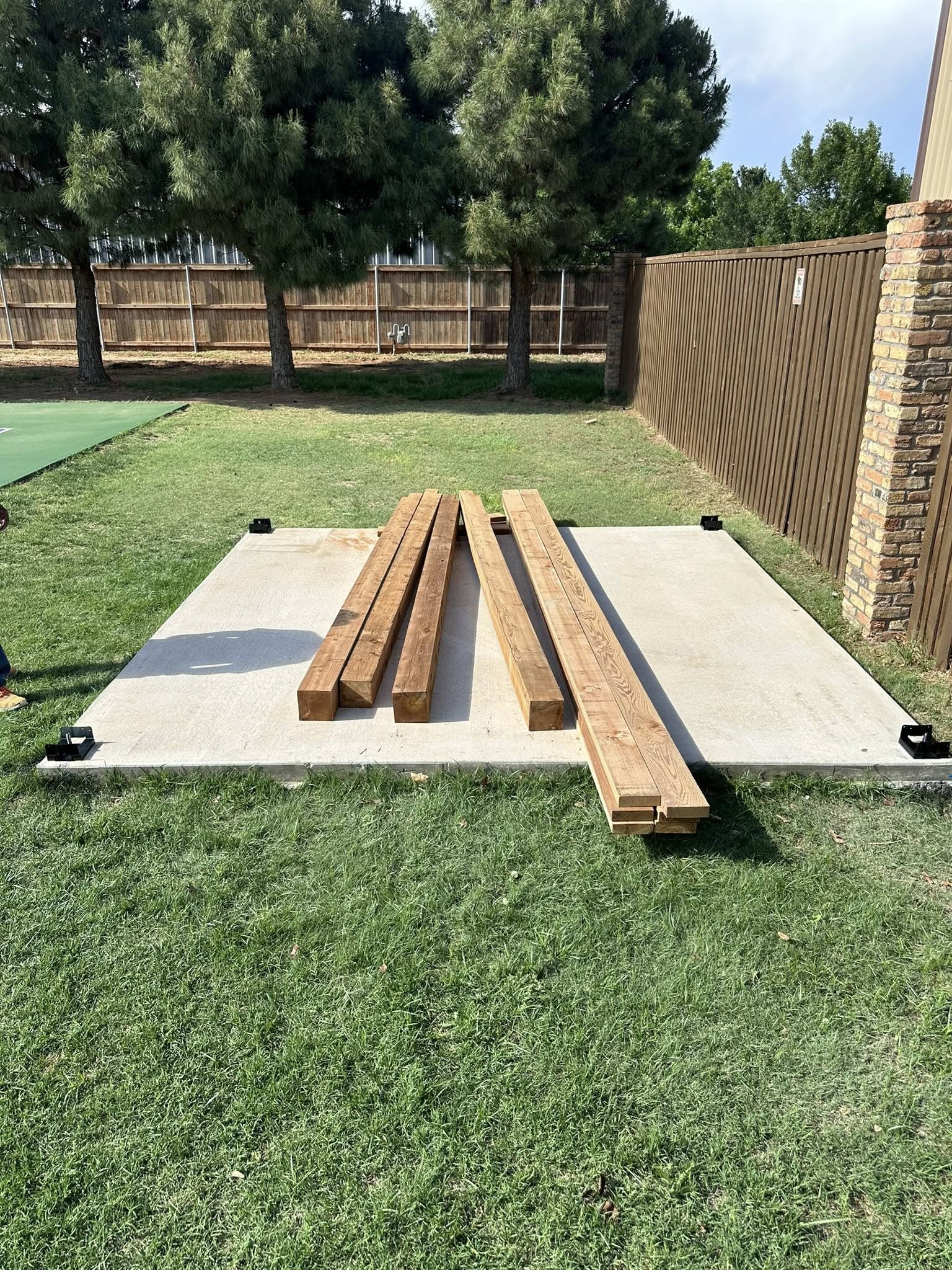 Four wooden boards on a concrete pad in a grassy backyard, with trees and a fence in the background.