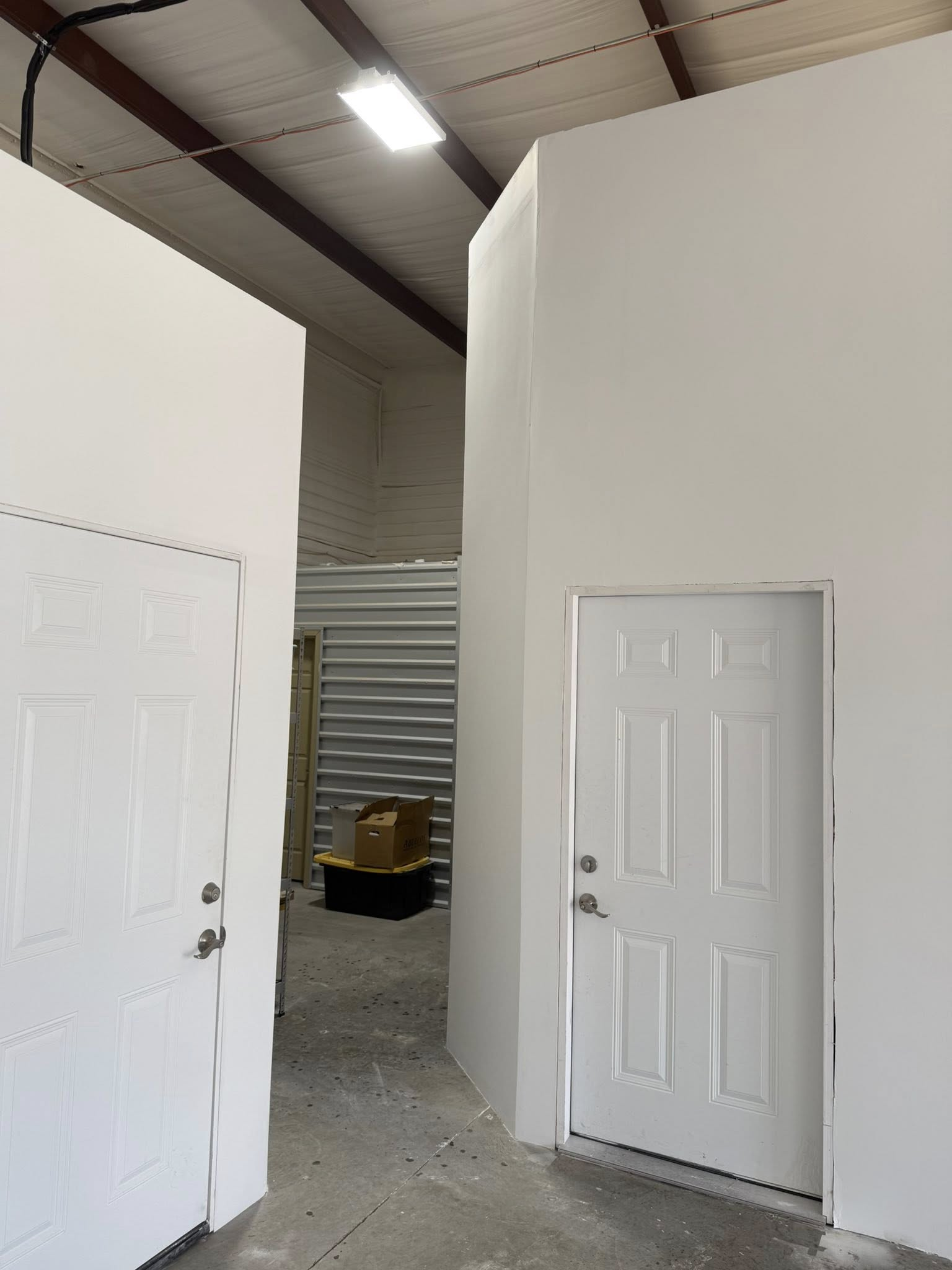 Interior view of two white walls with a door and a corrugated metal wall in the background.