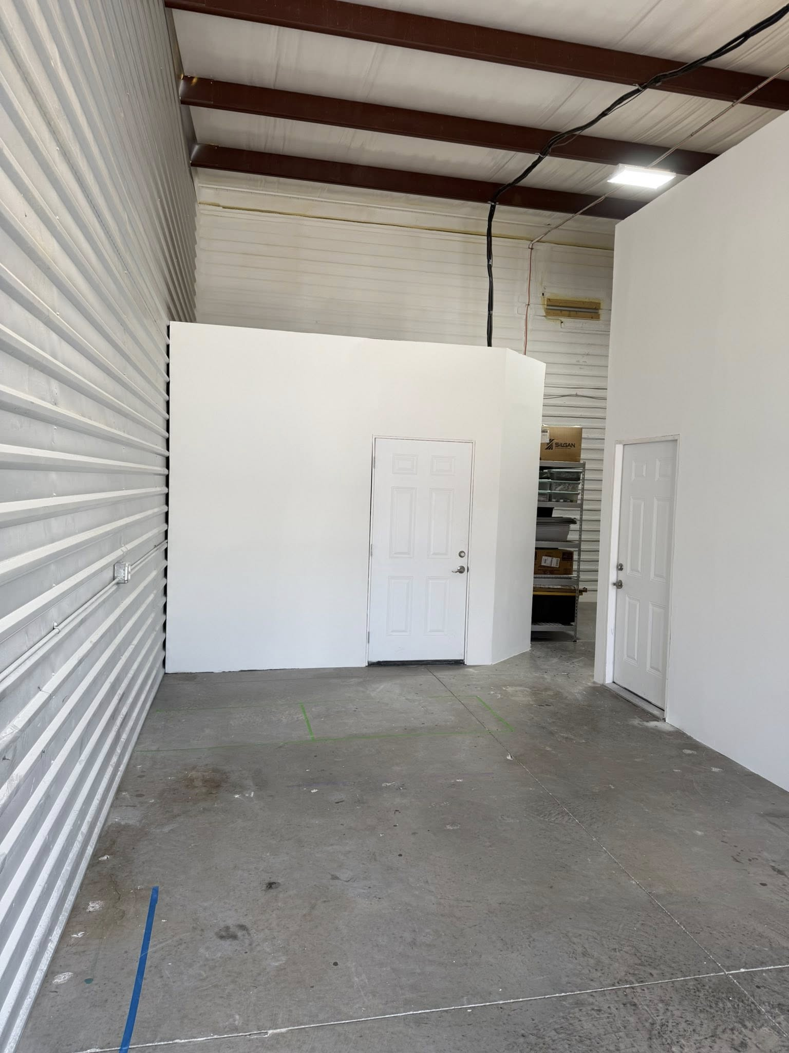 Empty white room with roll-up door, white walls, and a small doorway.
