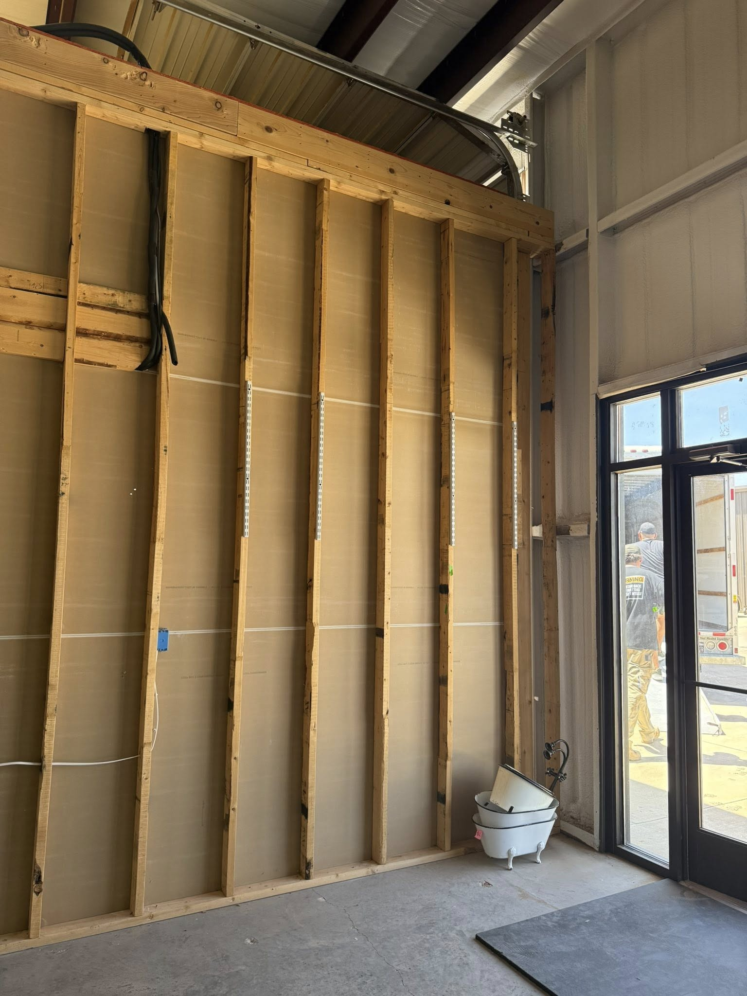 Interior wall framing with insulation, near a glass door and concrete floor.