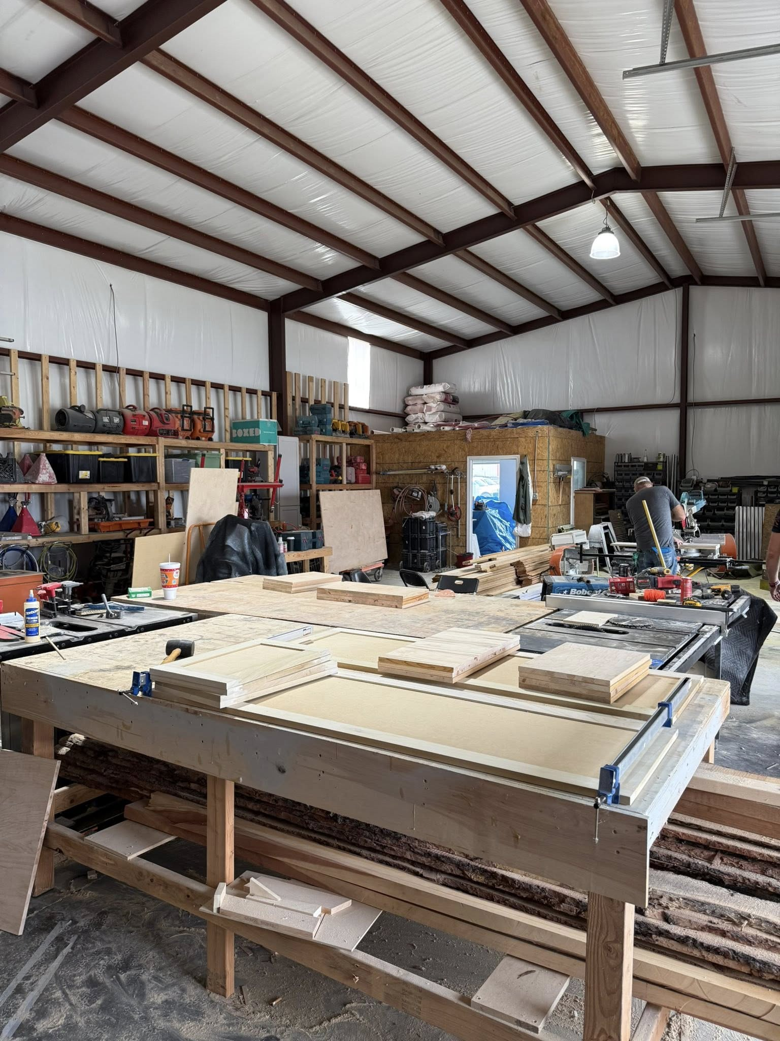 Workshop interior with woodworking tools, workbench, and lumber under a metal roof.