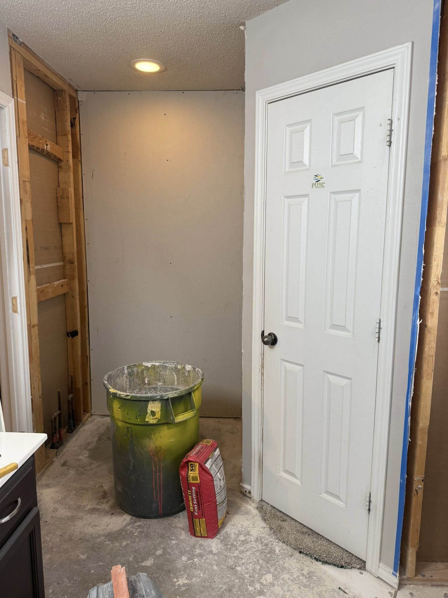 Bathroom under renovation, with exposed framing, a closed white door, and a trash can.