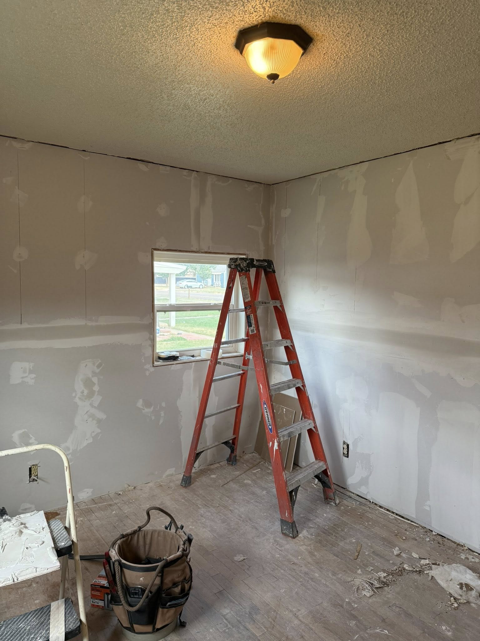 Room under construction with ladder near window, drywall visible, and tools on the floor.