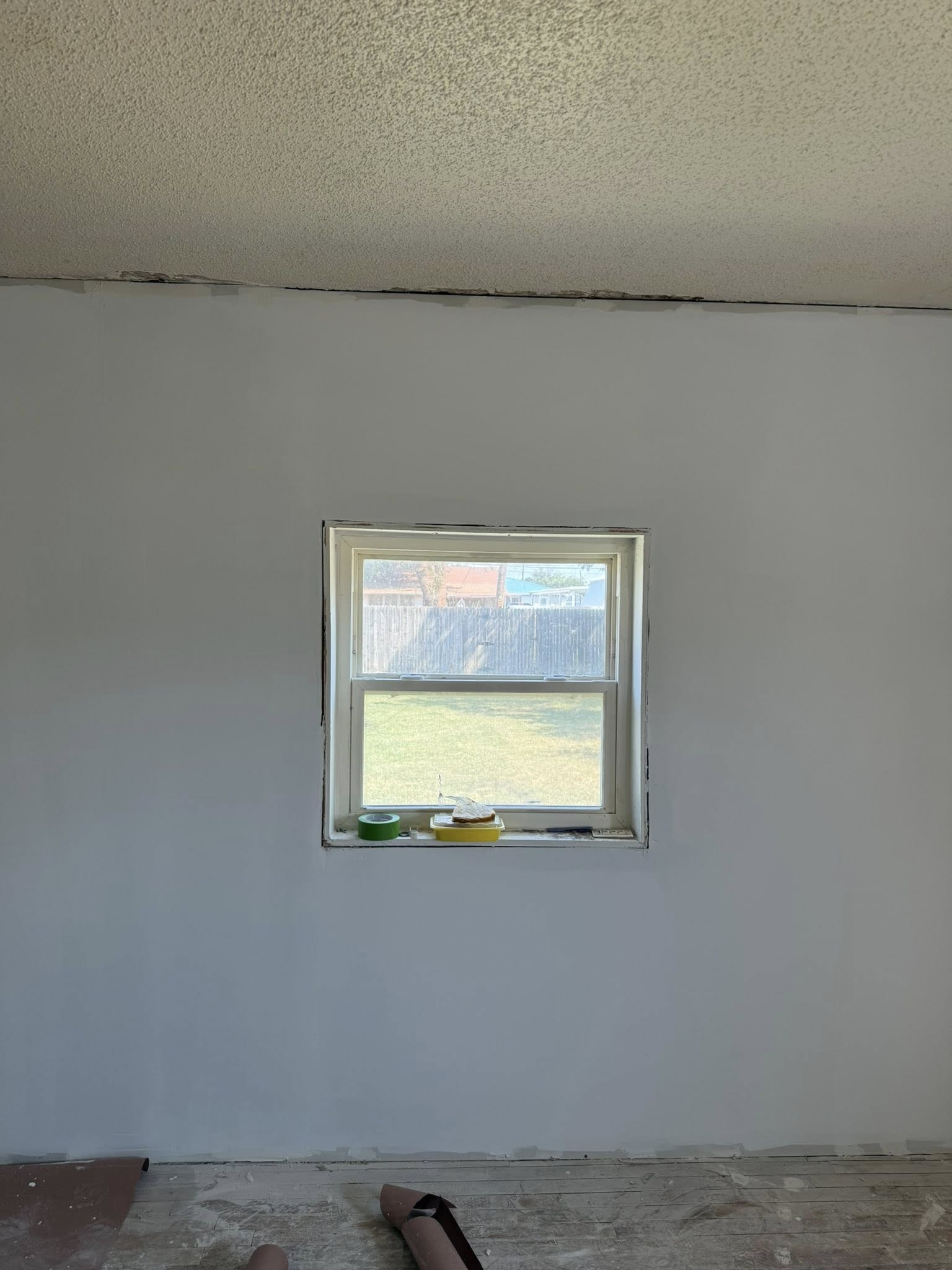Gray-painted wall with a square window centered, green grass and sky visible outside.