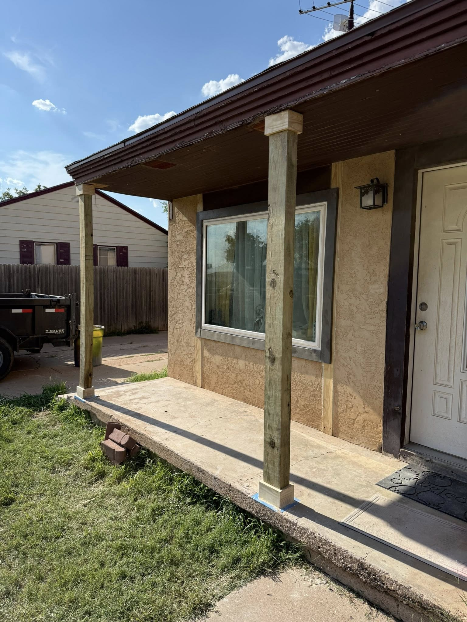 Porch of a house with wooden columns, concrete floor, and a window; sunny day.