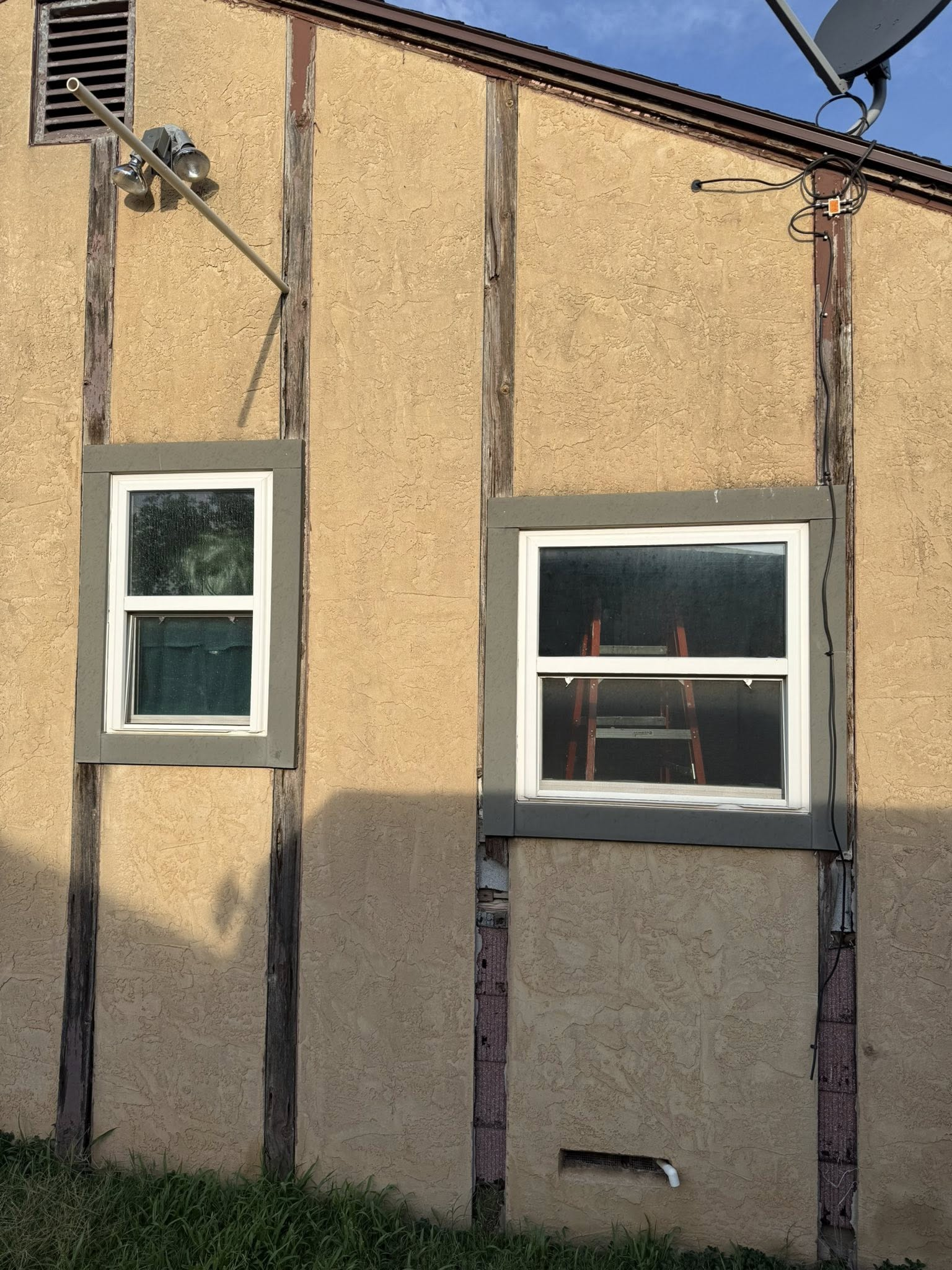 Two white-framed windows in a beige stucco wall, brown beams, and an antenna.