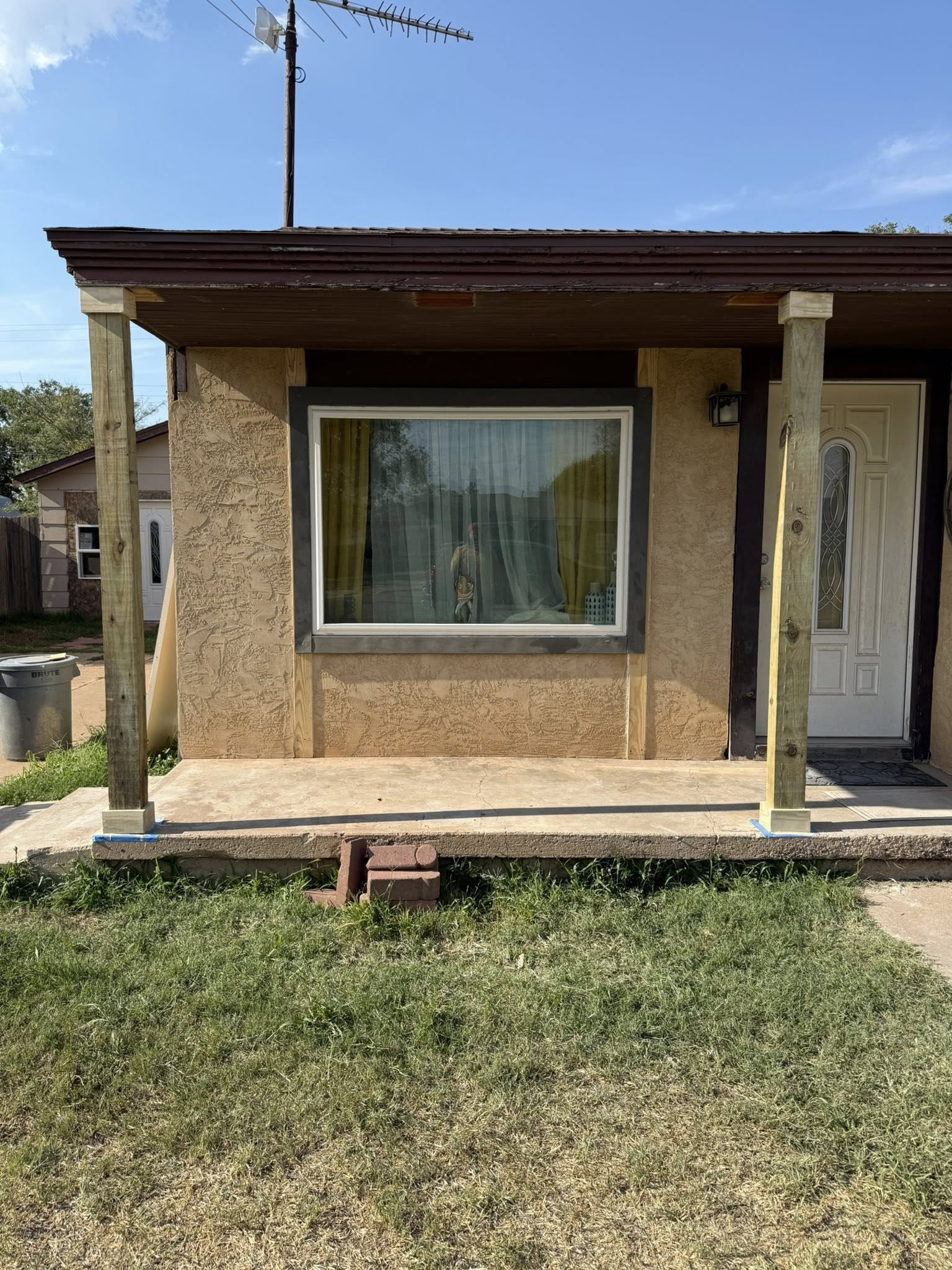 Tan house with porch and window; brown trim; two wooden support beams on porch.