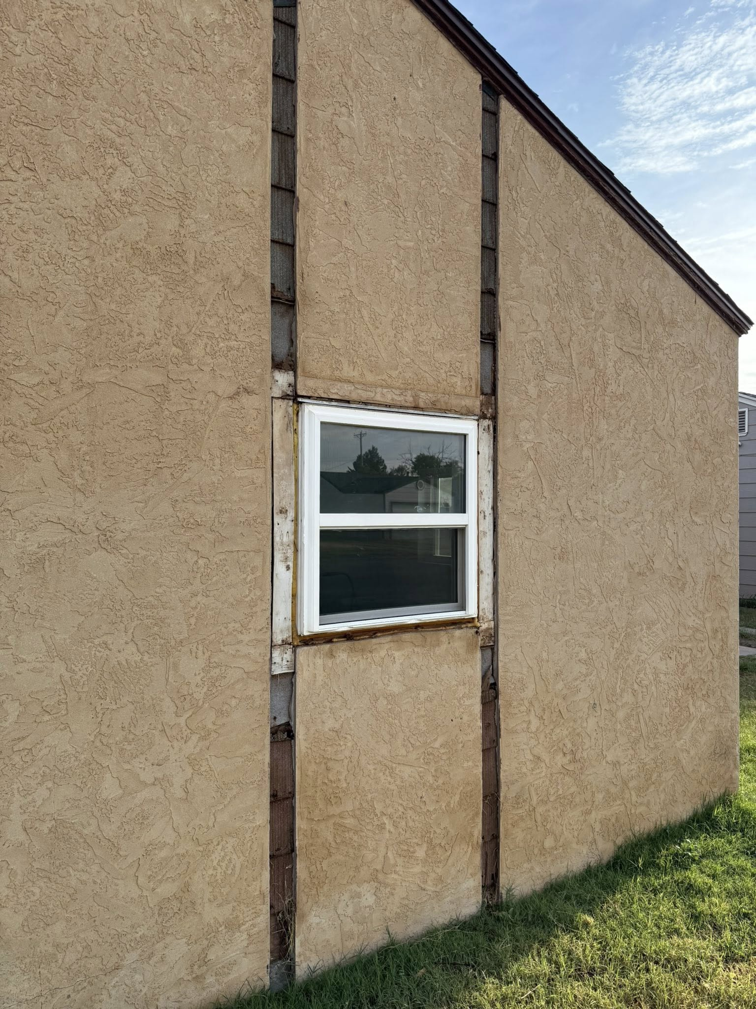 Tan stucco building with a white window. Brown trim lines the sides of the window. Green grass is at the bottom.