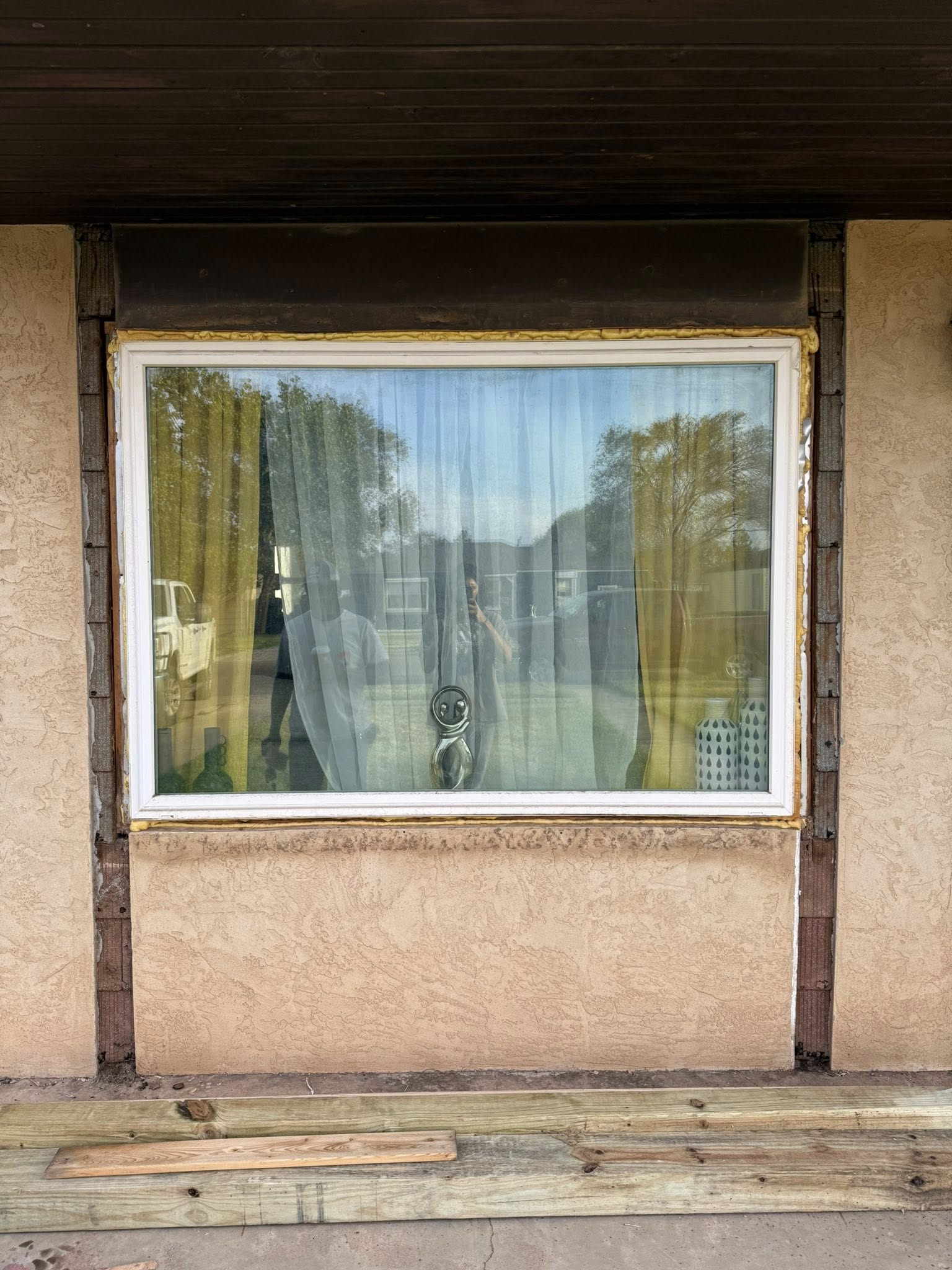 Window with roller shutter, white frame, sheer curtains, reflecting a yard.