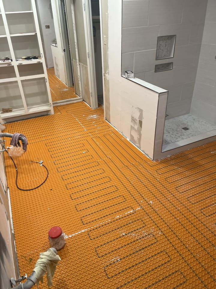 Orange floor heating system installed in a bathroom under construction; shower and doorway visible.