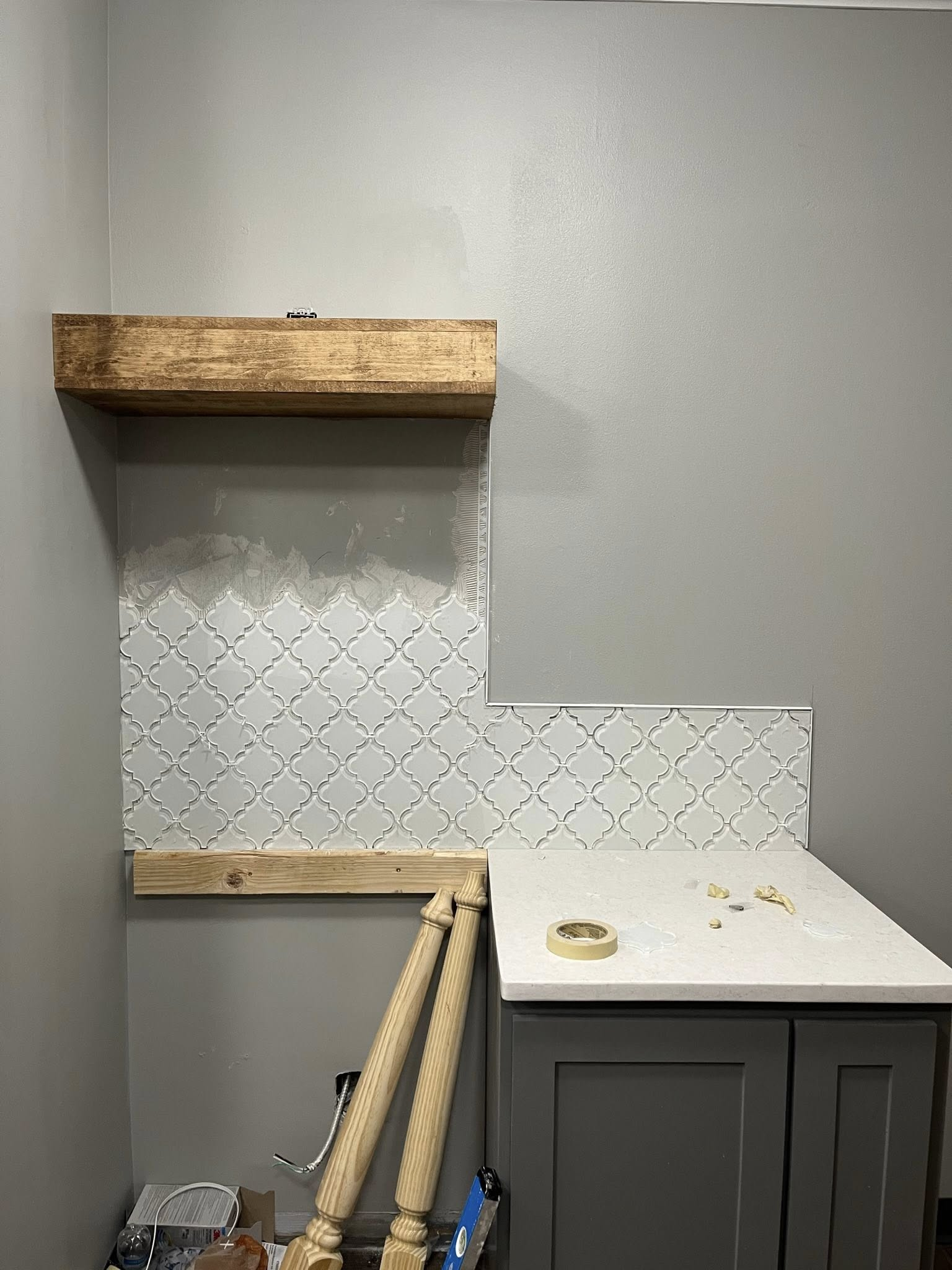 Gray kitchen with white countertop, silver tile backsplash, and a wooden shelf.