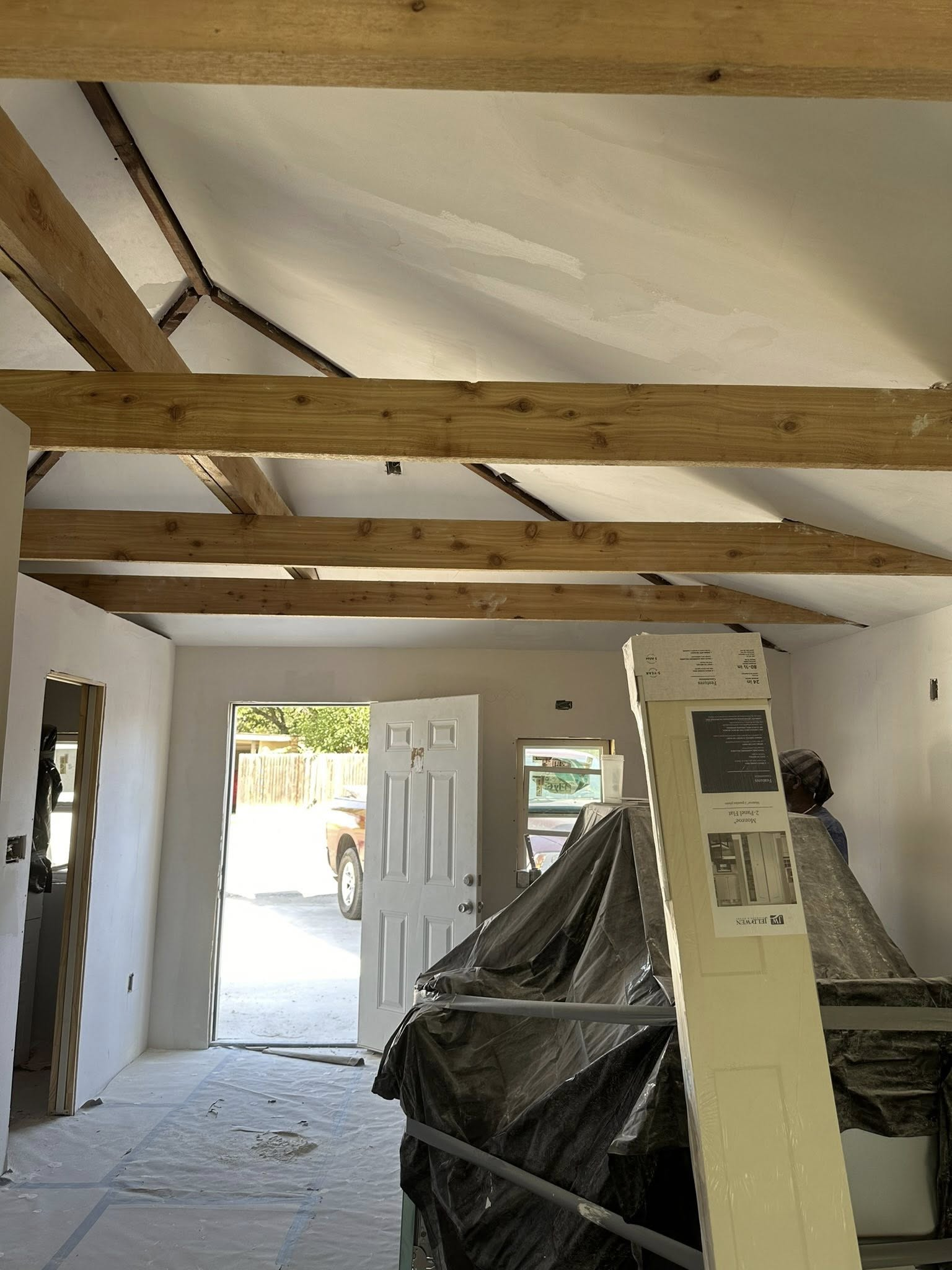 Interior of a room under construction, with wooden beams, an open door, and covered objects.