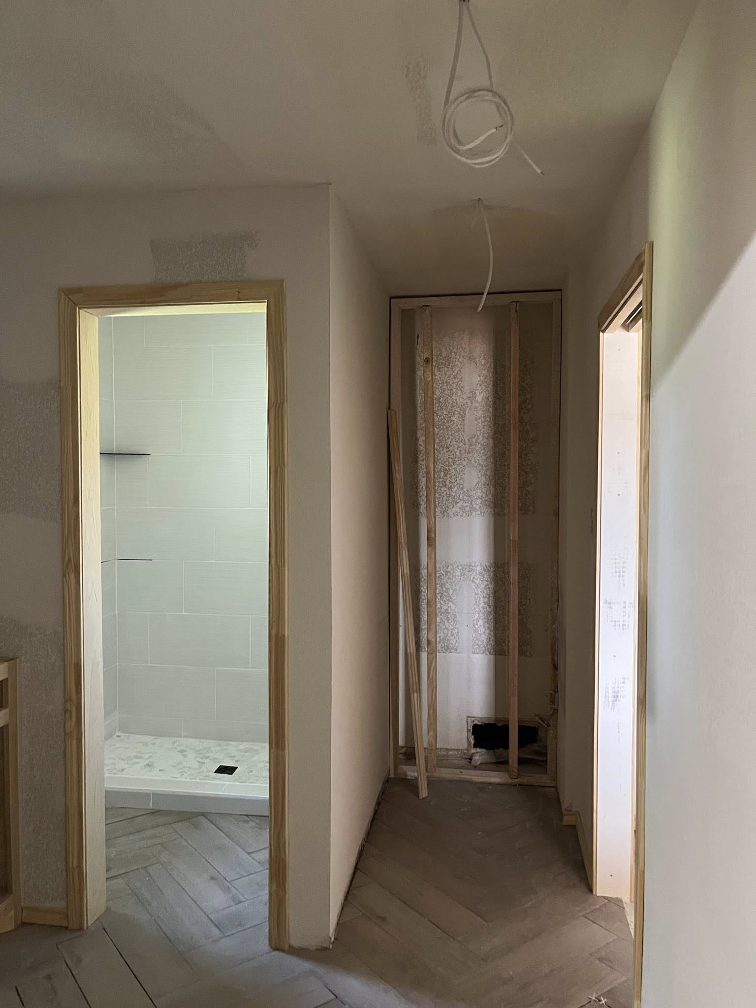 Hallway with open doorways to a bathroom and another room, with unfinished construction and exposed wires.