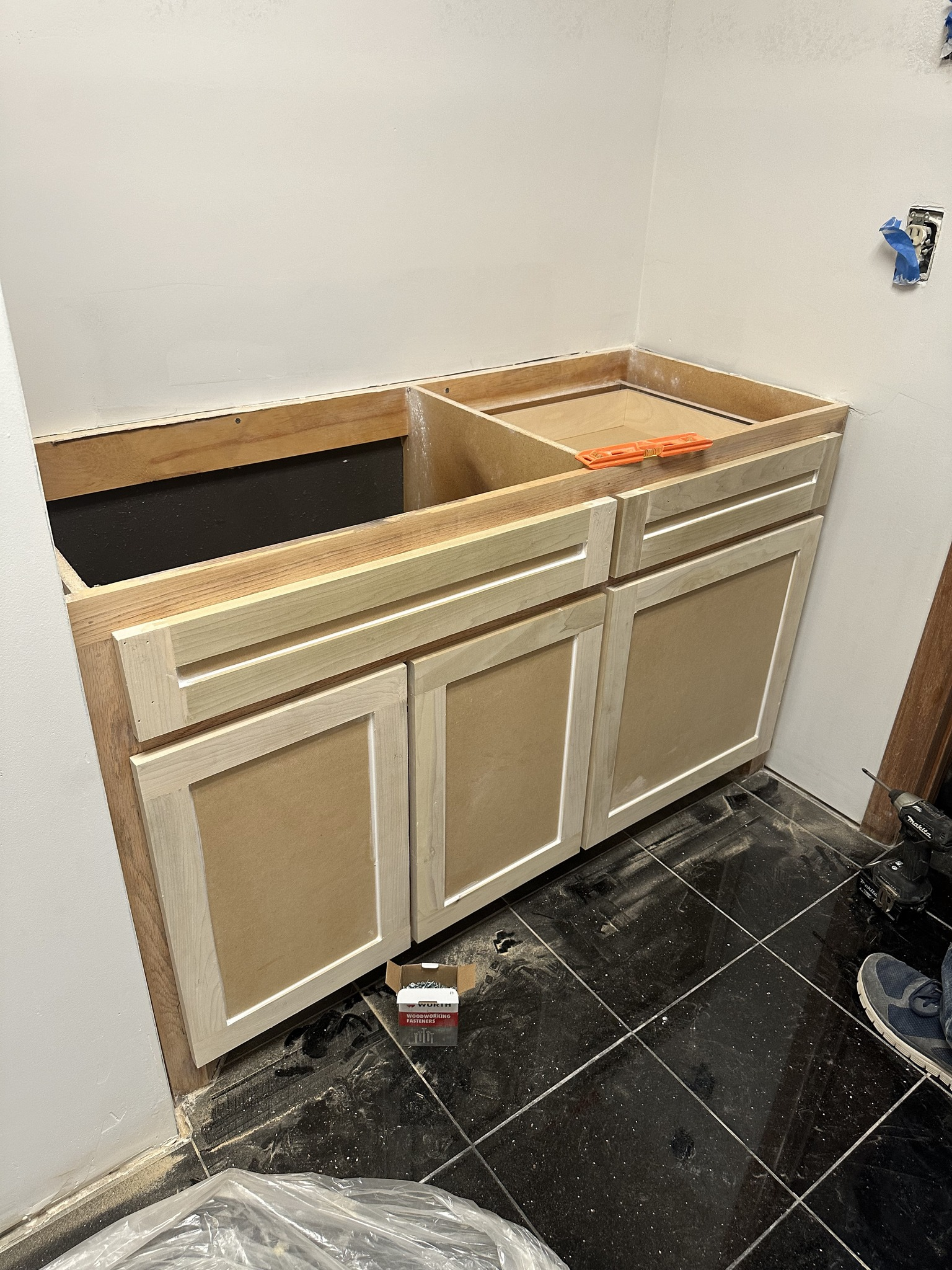 Unfinished light wood bathroom cabinet with two doors and an open top, against a white wall and tiled floor.