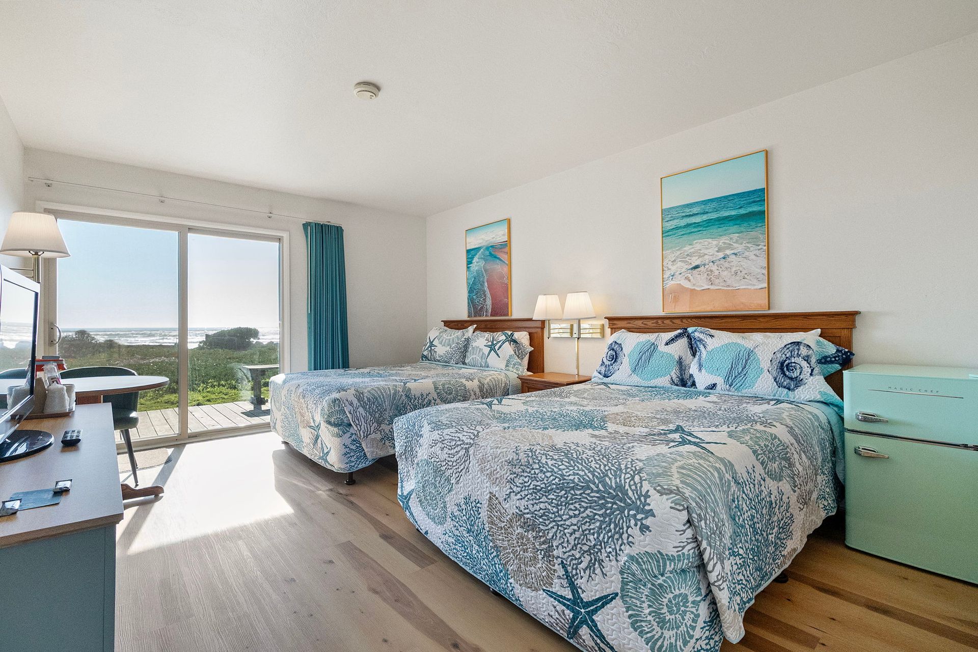Bright hotel room with two beds, a sliding door to an outdoor view, and simple decor.