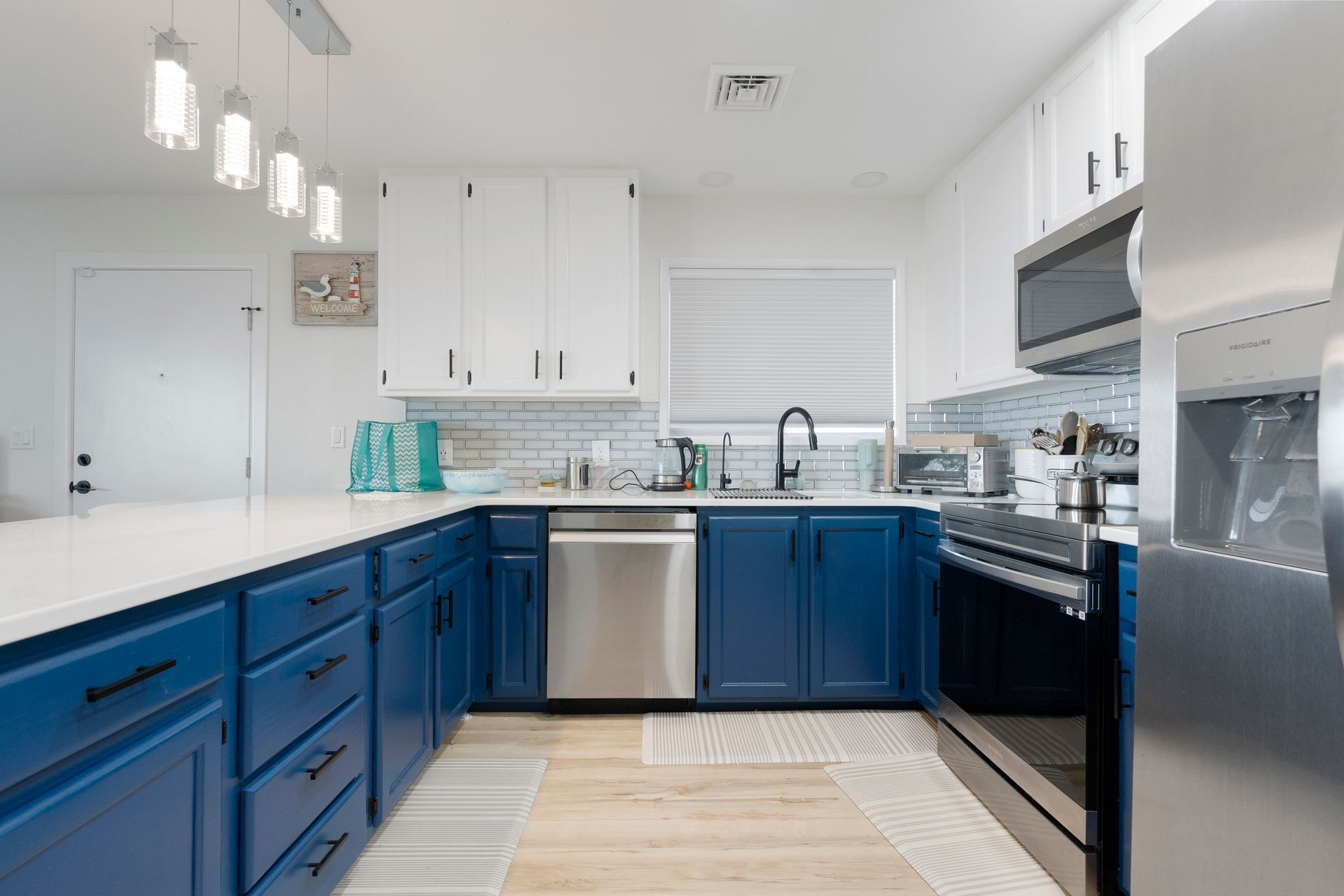 Blue and white kitchen with white countertops, stainless steel appliances, and blue cabinetry.