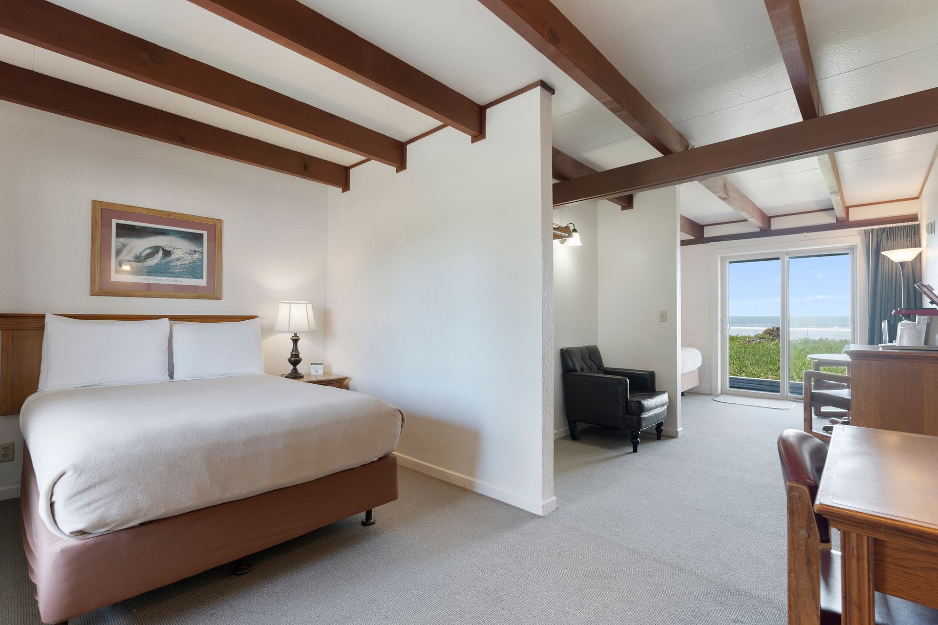 Hotel room with a bed, armchair, desk, and ocean view.
