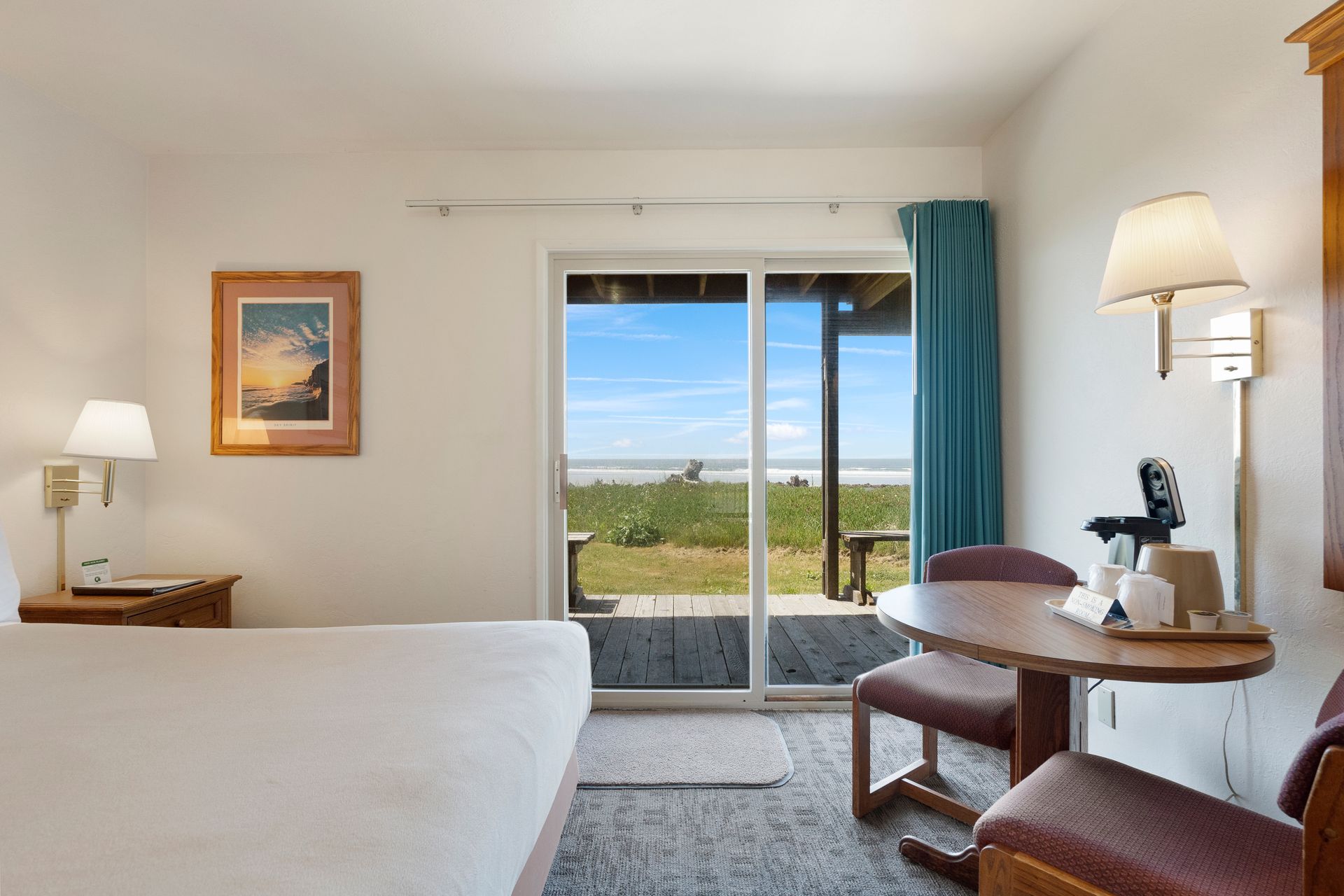 Motel room with ocean view, featuring a bed, table, chairs, and sliding glass door.
