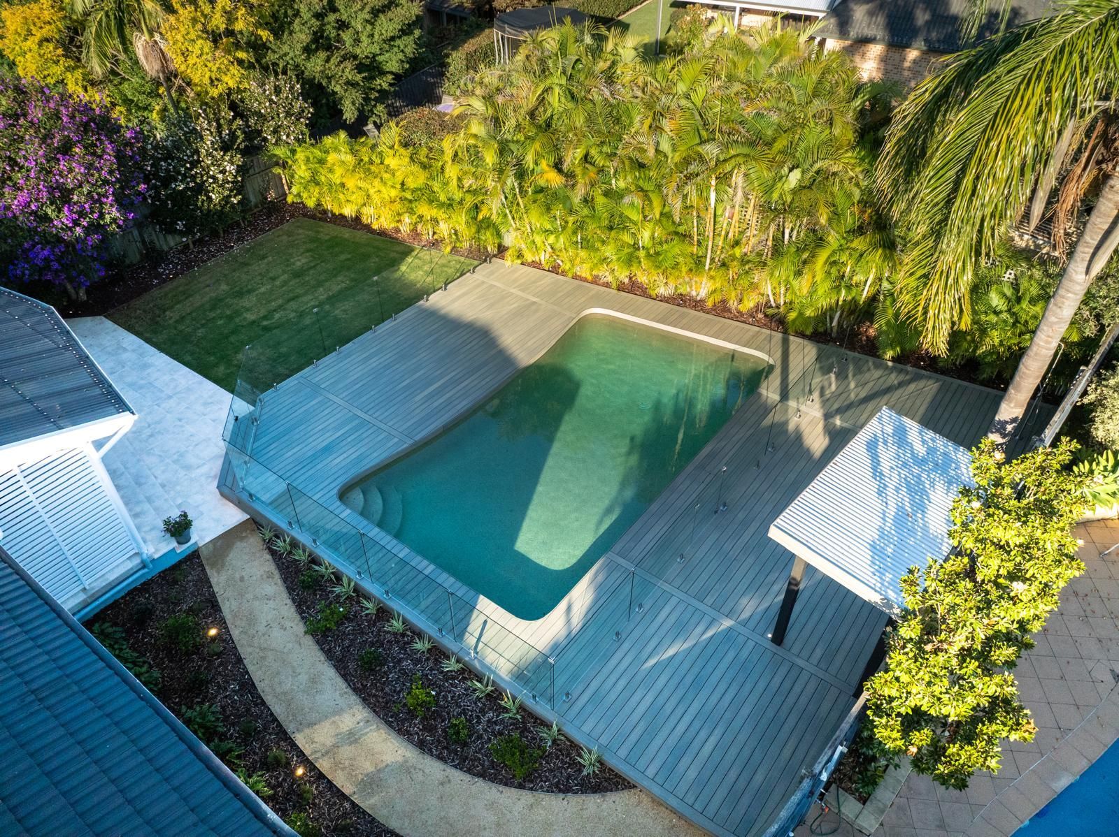 An aerial view of a large swimming pool in a backyard surrounded by trees.