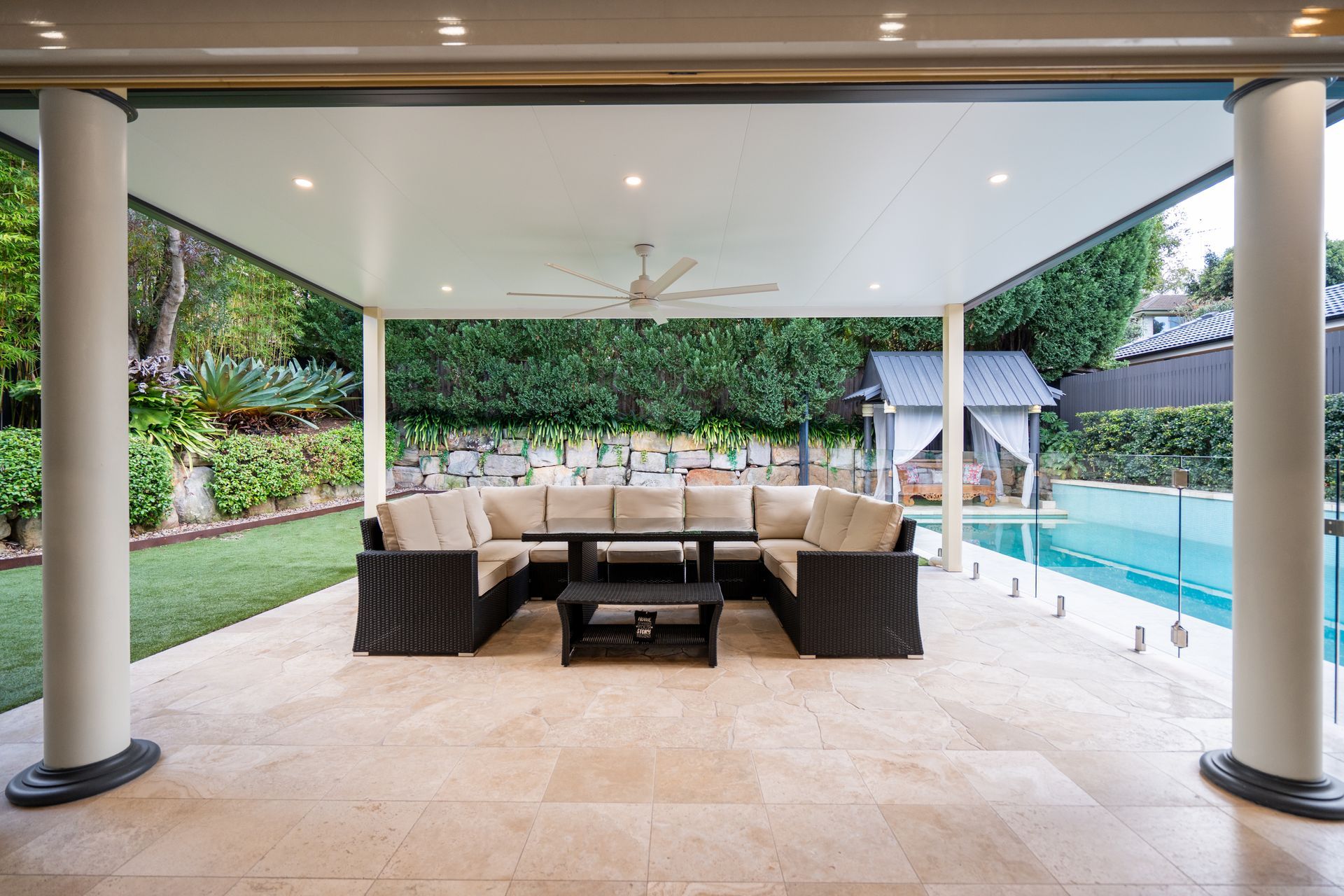A patio with a table and chairs under a canopy overlooking a swimming pool.