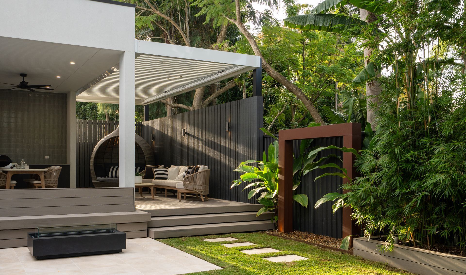 Outdoor patio with seating, wooden deck, pergola, and lush greenery.