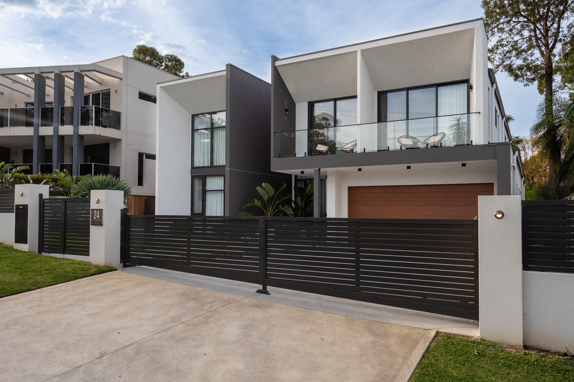 Modern two-story house with dark gray exterior, brown garage door, and decorative black fence.