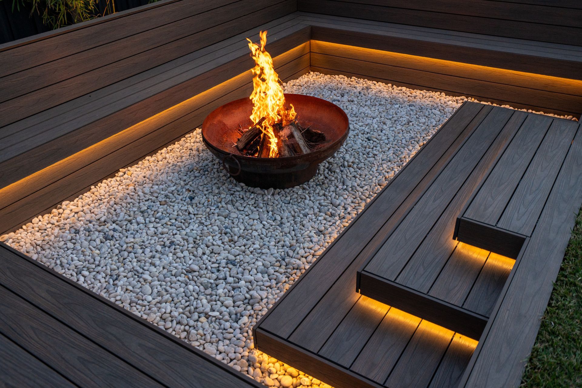 A sunken fire pit is surrounded by timber decking and pebbles. 