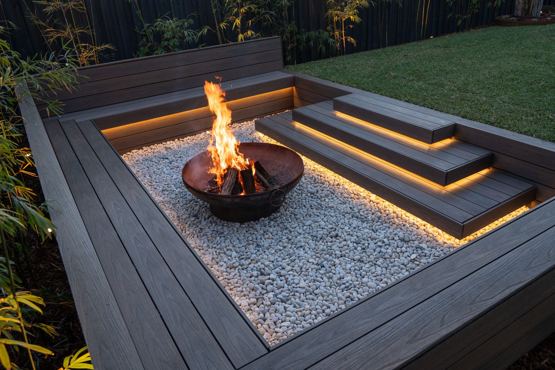 A sunken fire pit is surrounded by timber decking and pebbles. 