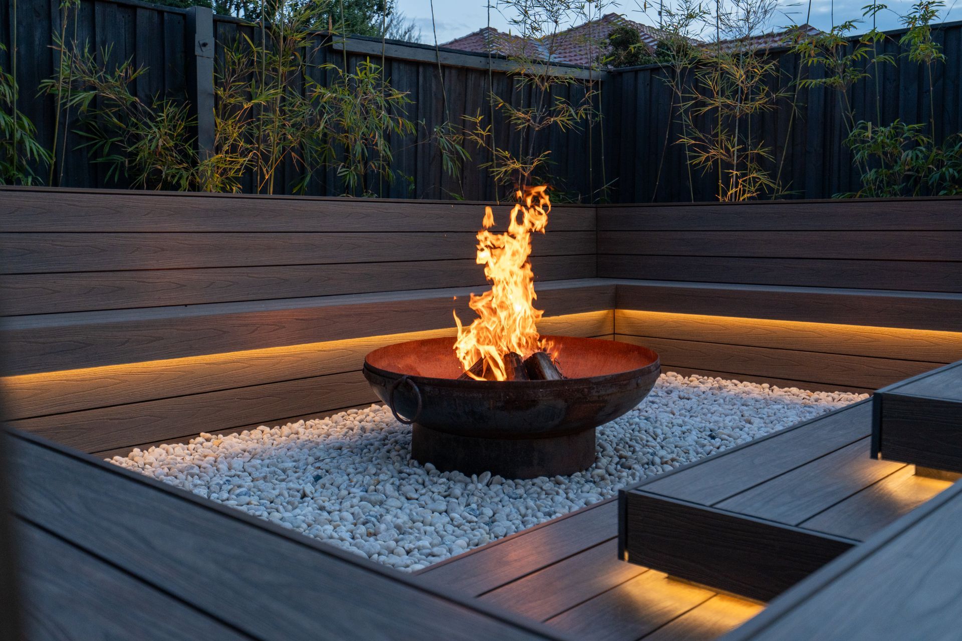 A sunken fire pit is surrounded by timber decking and pebbles. 