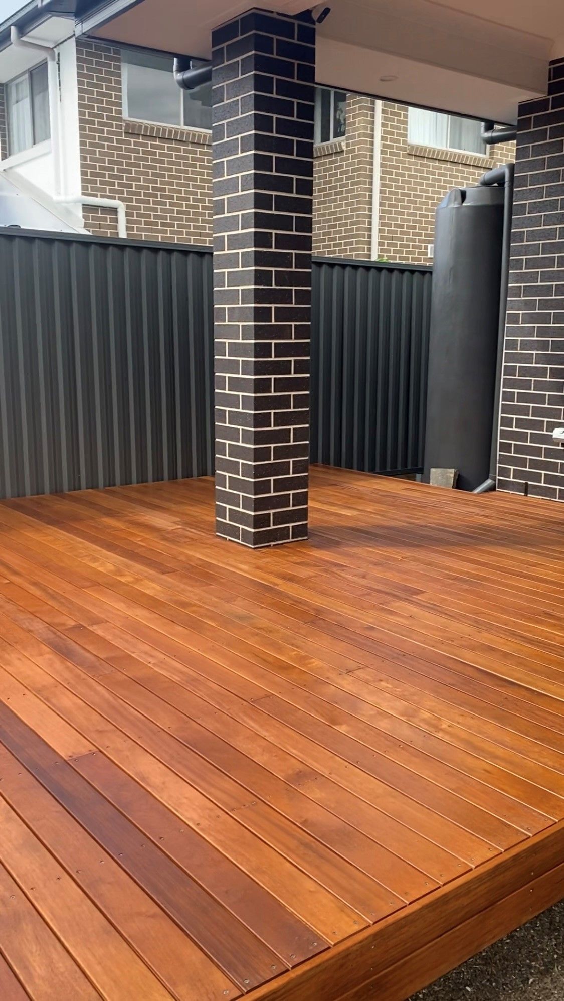 A wooden deck with a brick wall and a fence in the background.