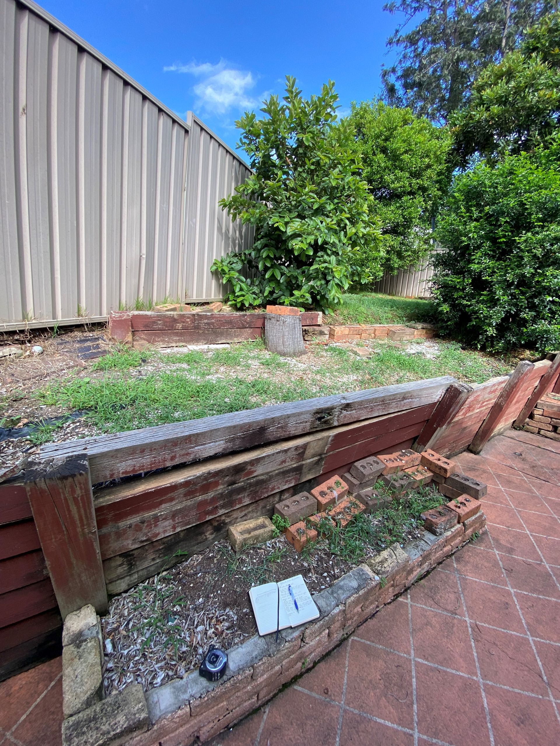 There is a brick walkway in the backyard with a fence in the background.