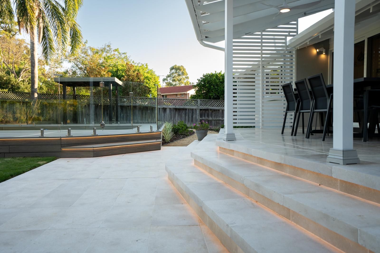 A patio with stairs leading up to a house and a pool.