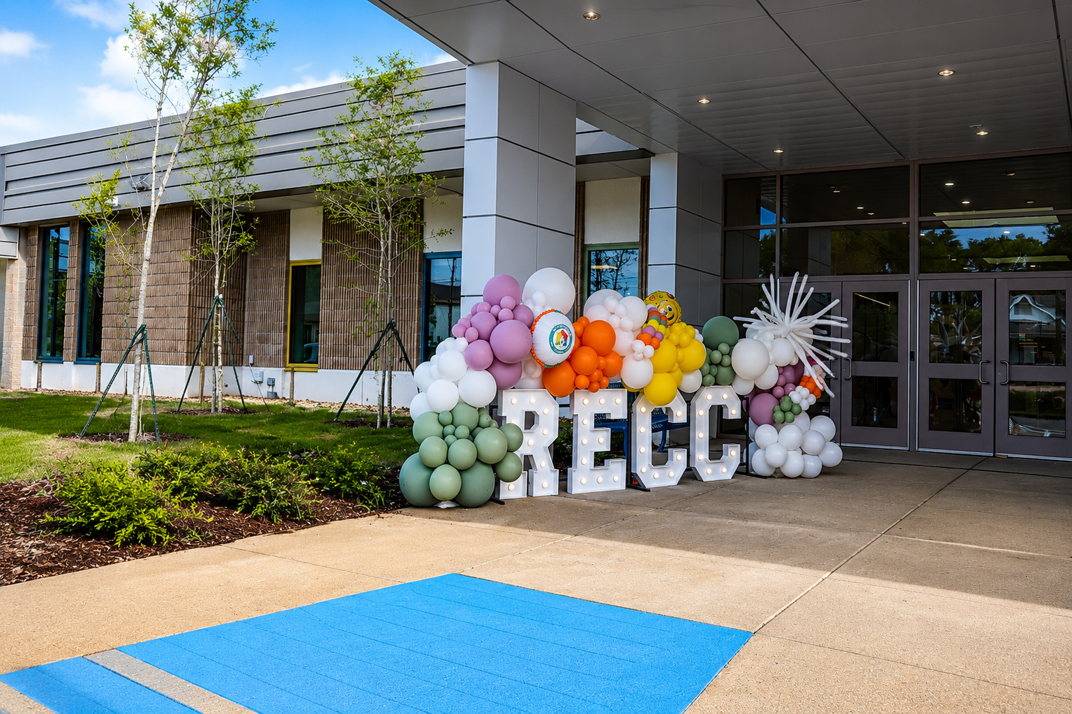 Outdoor entrance with colorful balloon display and large “RECC” letters in front of a building