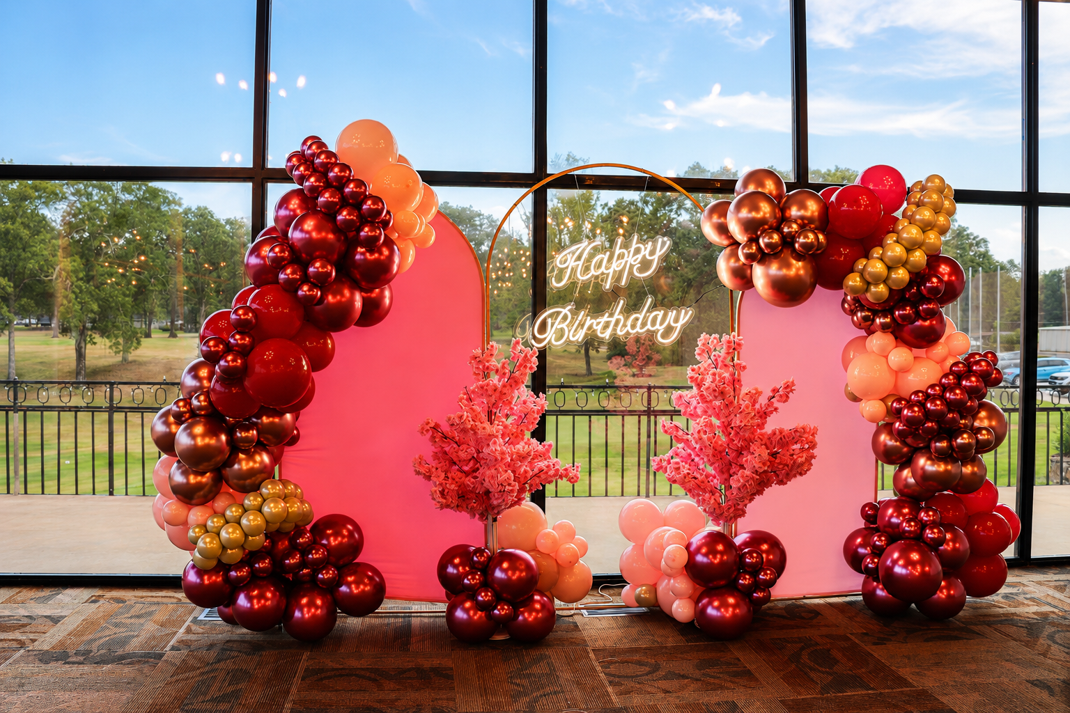 Pink and gold balloon birthday arch with gift boxes in front of large windows
