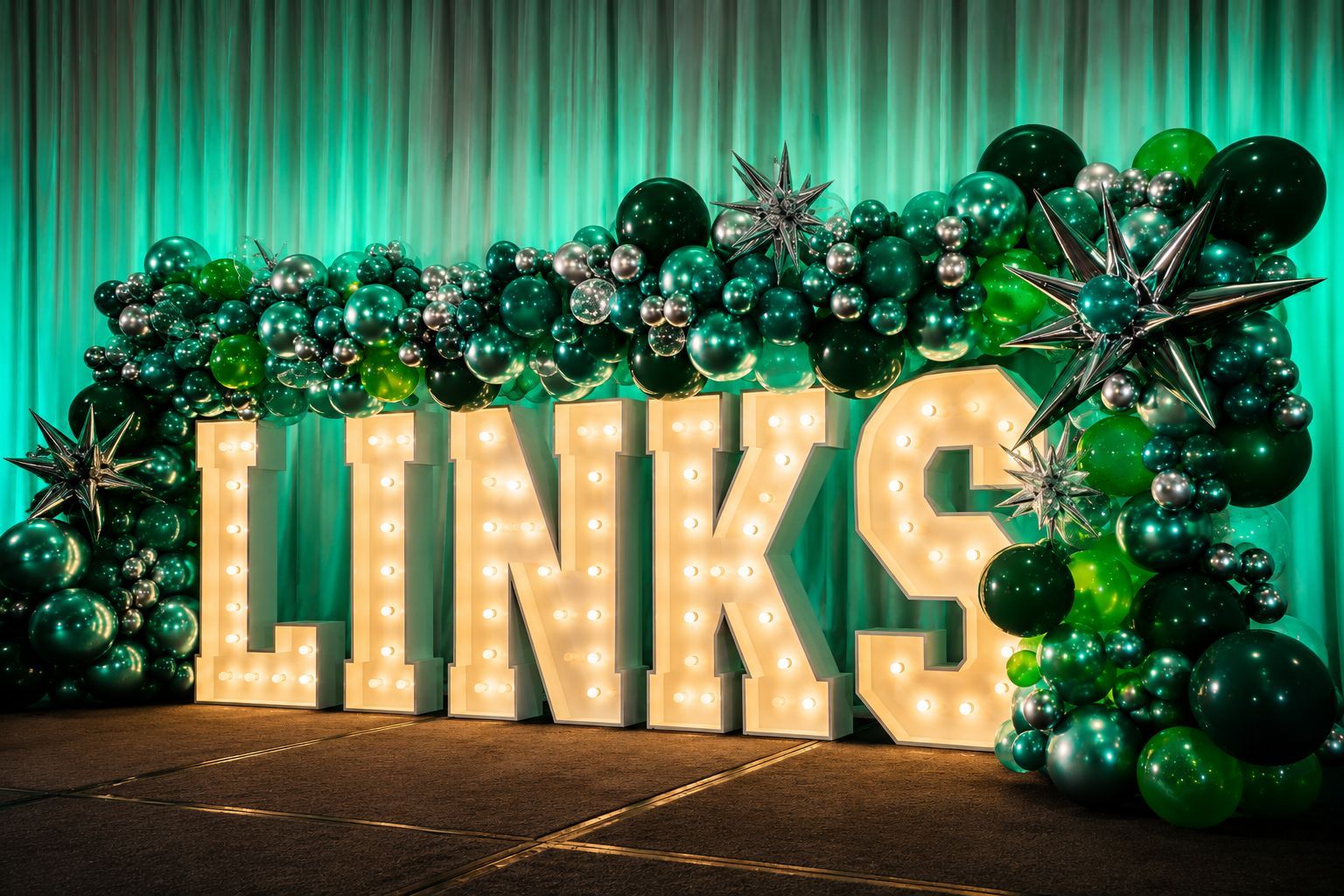 Illuminated “LINKS” marquee letters with green balloon garland on a stage with teal drapes