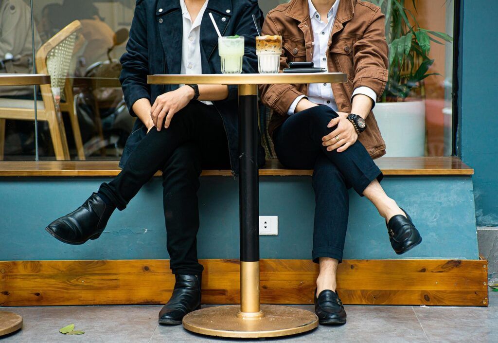 Two people seated at a table, enjoying drinks. One wears a black jacket, the other a brown one.