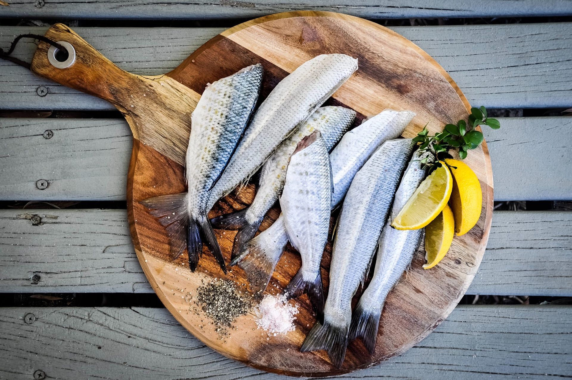 Raw fish fillets on a wooden cutting board with lemon slices, herbs, and seasonings.