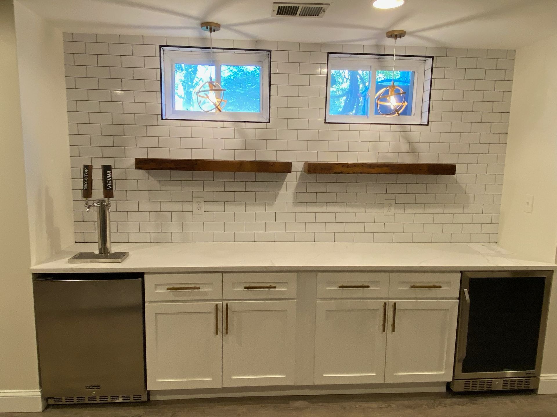 Modern kitchen with white cabinets, tile backsplash, white countertop, and two small windows above open shelves.