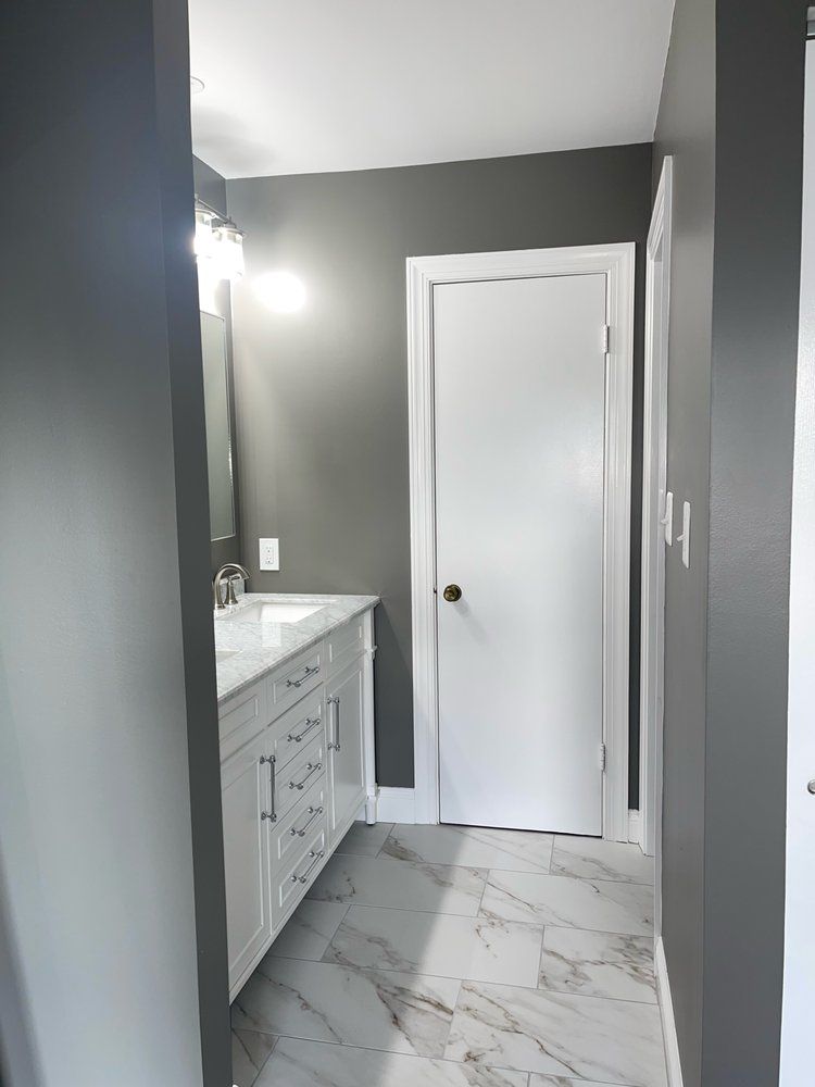 A bathroom with gray walls and white cabinets and a white door.