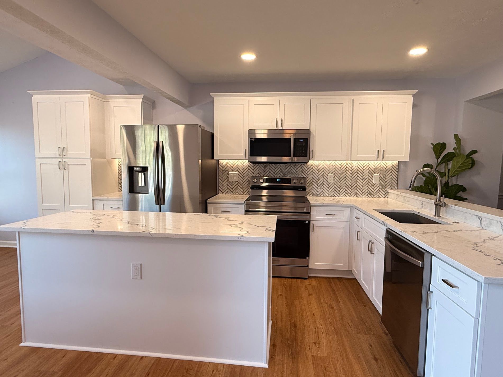 Bright modern kitchen with white cabinets, stainless appliances, marble island, and wood floor