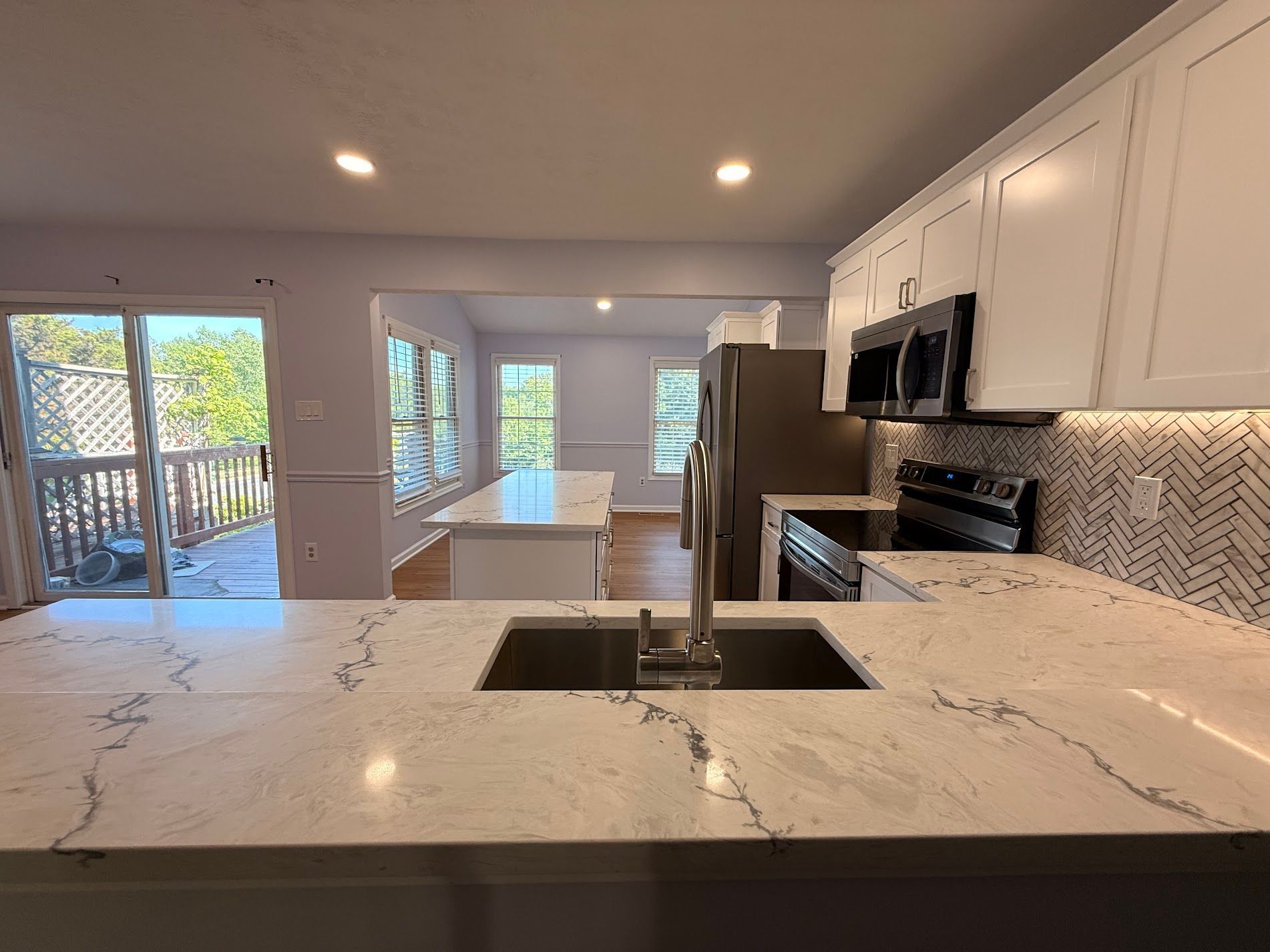 Bright modern kitchen with white cabinets, marble island, and stainless steel appliances looking into a living area