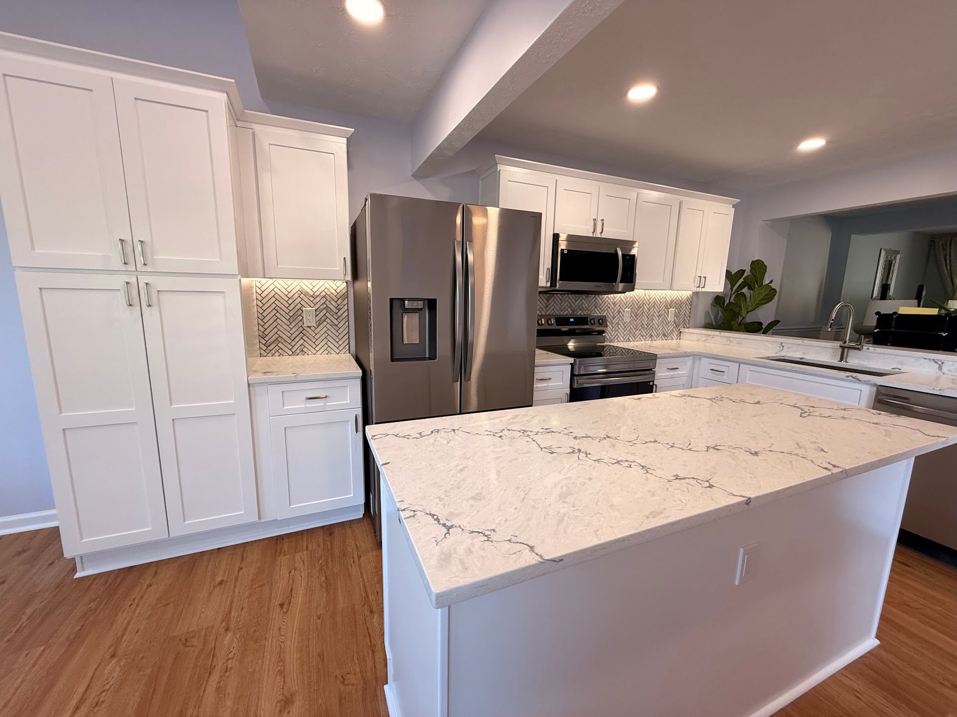 Bright modern kitchen with white cabinets, marble island, stainless steel appliances, and wood floors