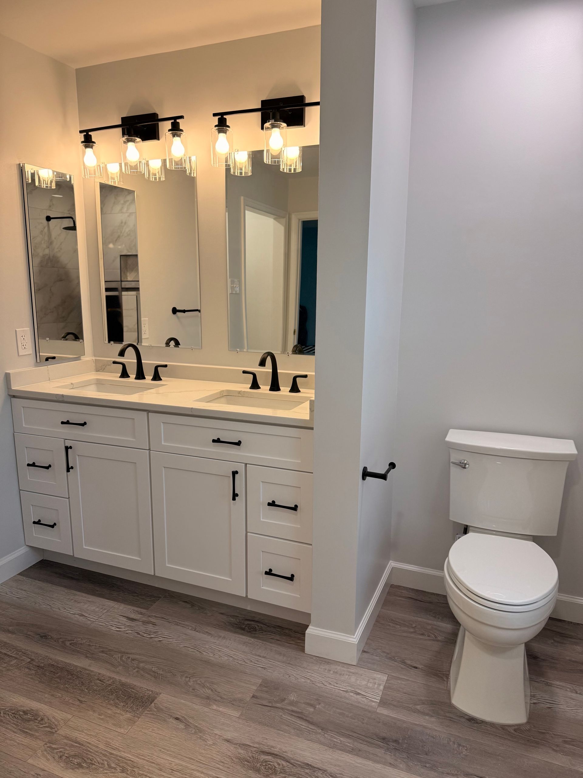 Bathroom vanity with triple mirrors and lights beside a white toilet on wood-look flooring