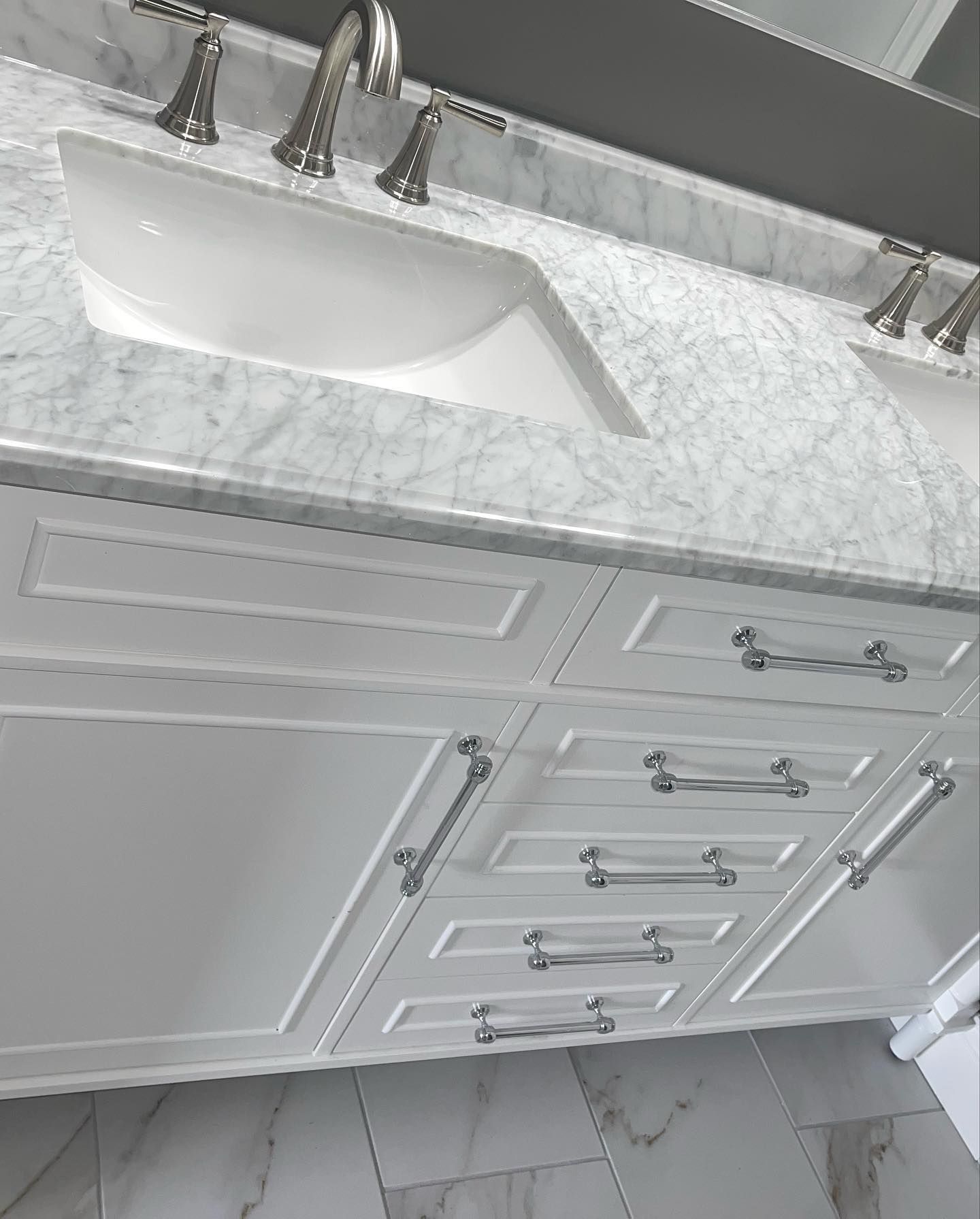 A bathroom sink with a marble counter top and white cabinets.
