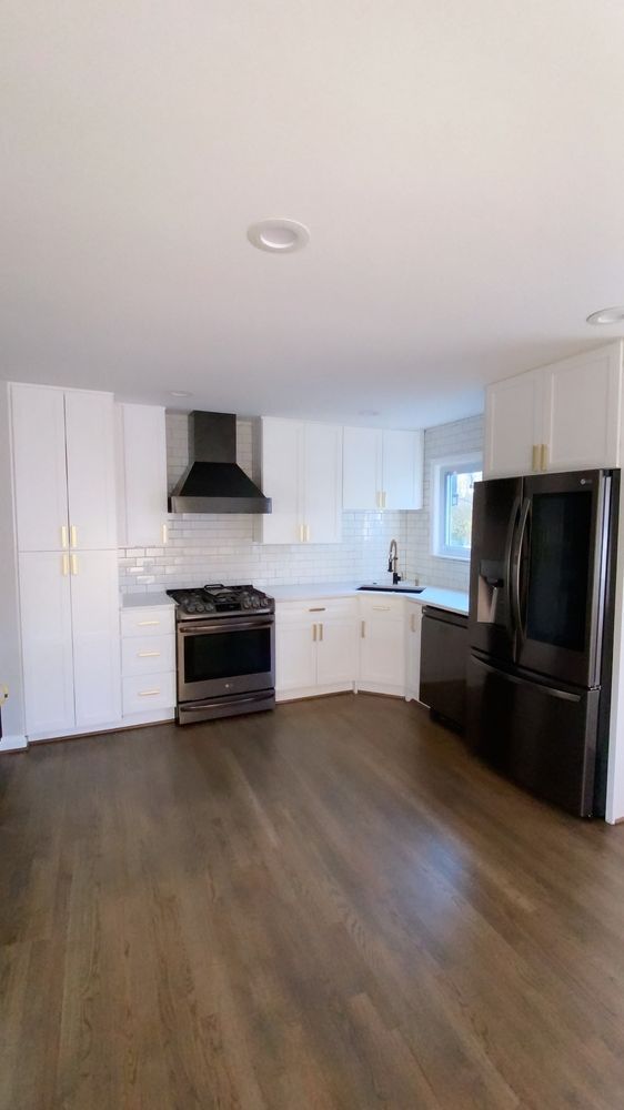 A kitchen with white cabinets , a black refrigerator , a stove , and a sink.