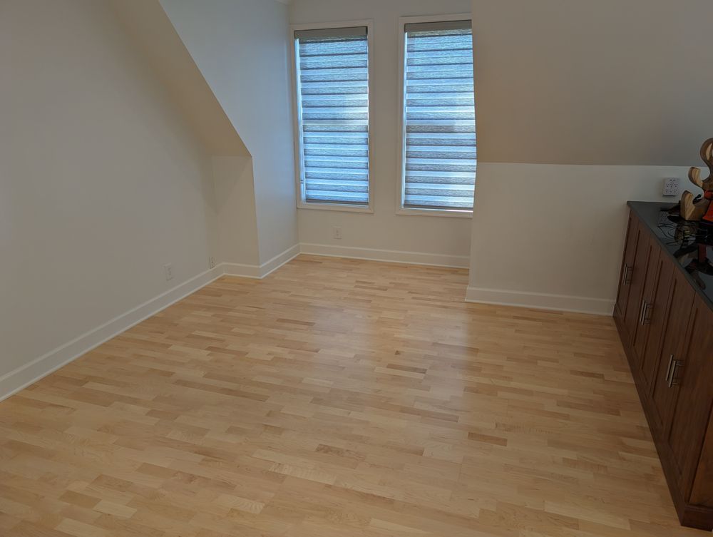 An empty room with hardwood floors and two windows.