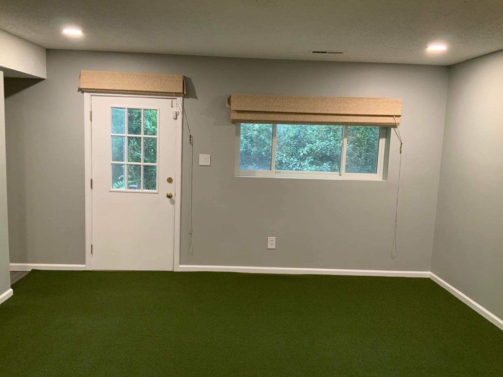 An empty room with a green carpet and a window.