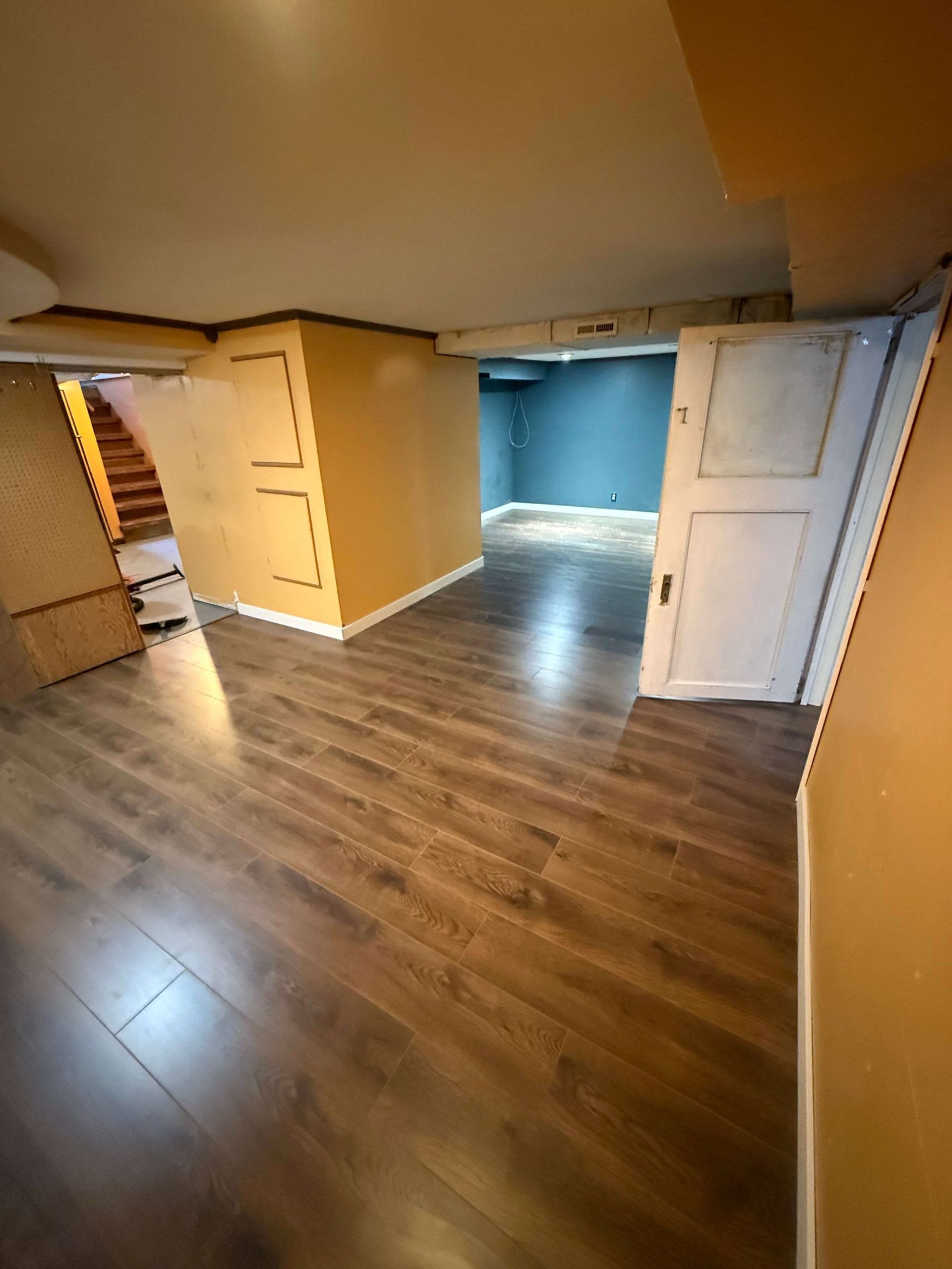 Empty room with wood floors, white doors, and blue-lit doorway under low ceilings