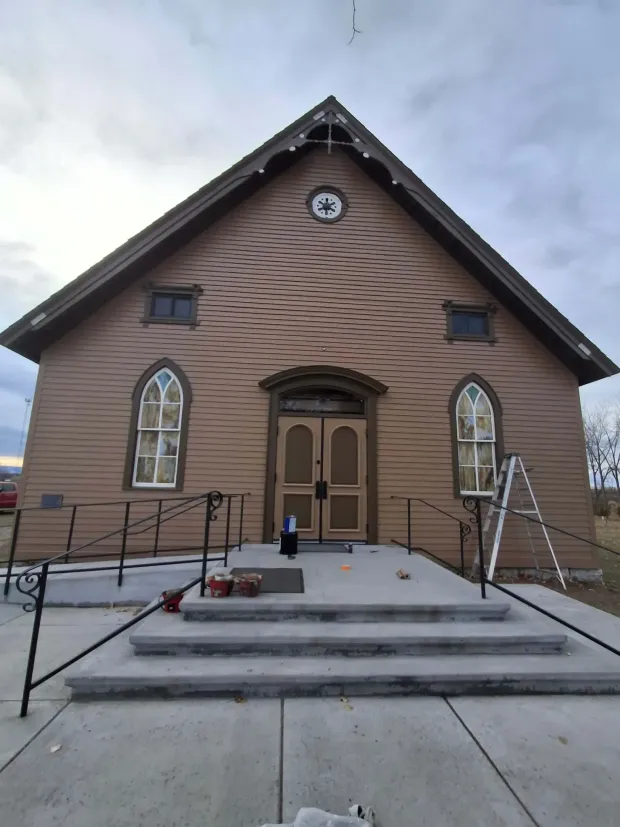 Front view of a small brown wooden building with arched windows and steps leading to the door