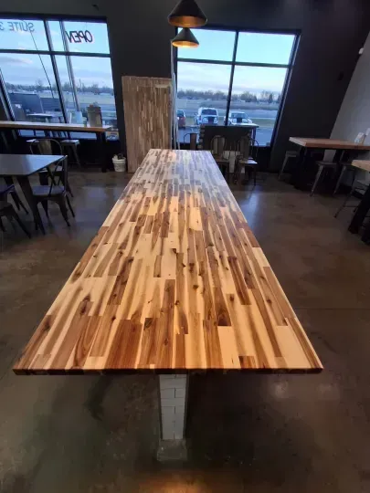 Long wooden communal table in a dim café with chairs and large windows